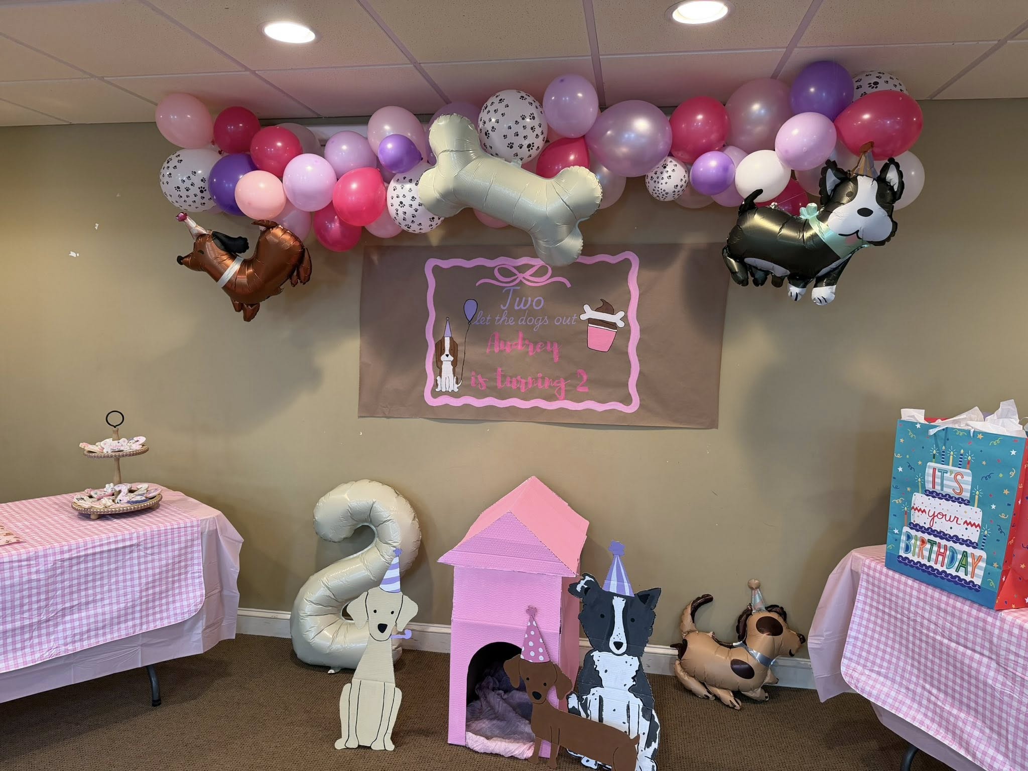 Dog-themed second birthday party decorations with balloons, a sign reading 'Audrey is turning 2', and dog cutouts.