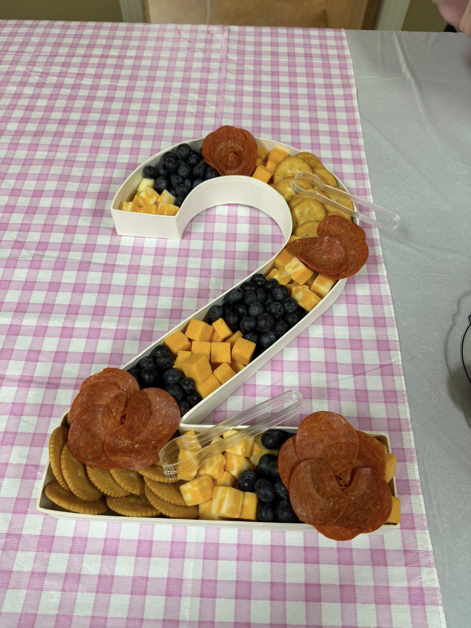 Charcuterie board filled with cheese, blueberries, crackers, and pepperoni shaped like the number two.