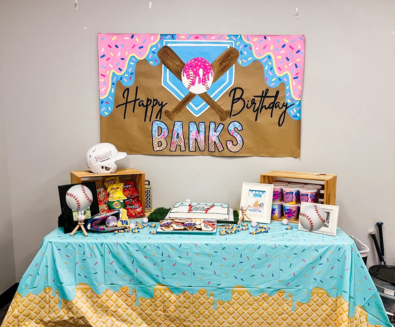 Baseball and donut themed birthday party table with a personalized birthday banner and treats.