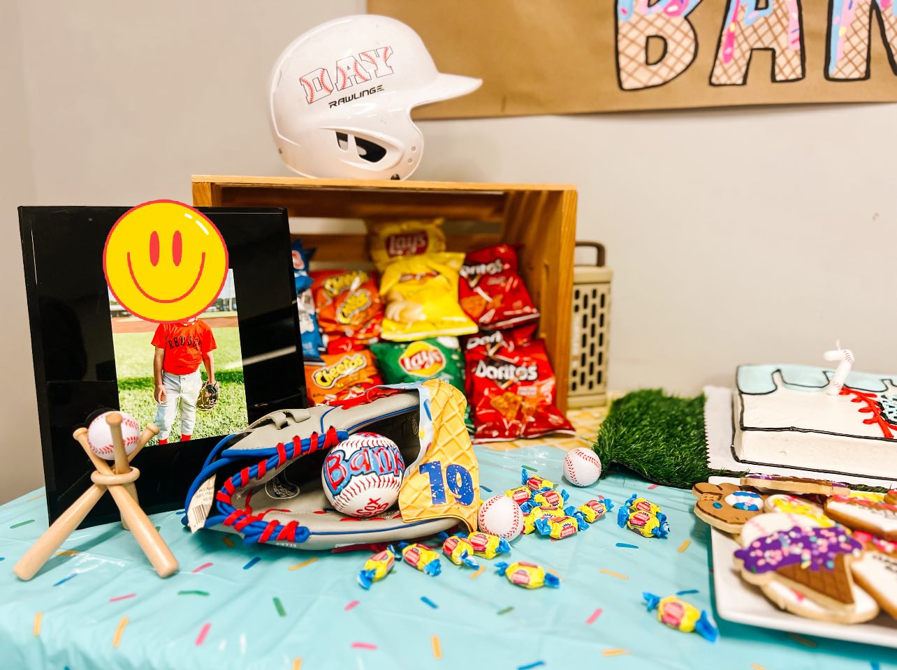Baseball-themed birthday party table featuring a Rawlings helmet, baseball glove, treats, and a photo frame.