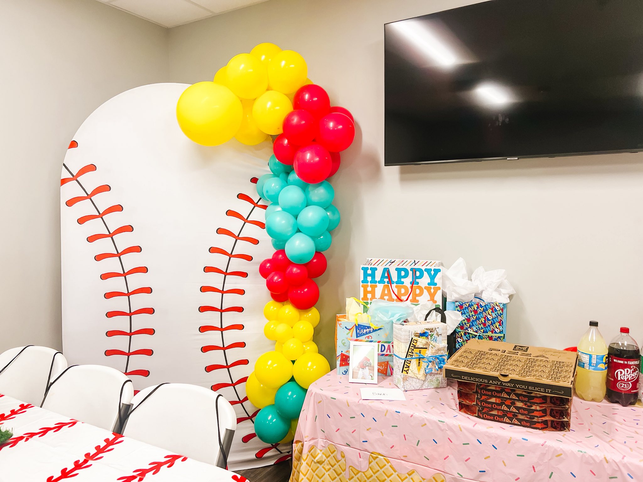 Baseball themed party decoration with a balloon arch and gifts on a table.