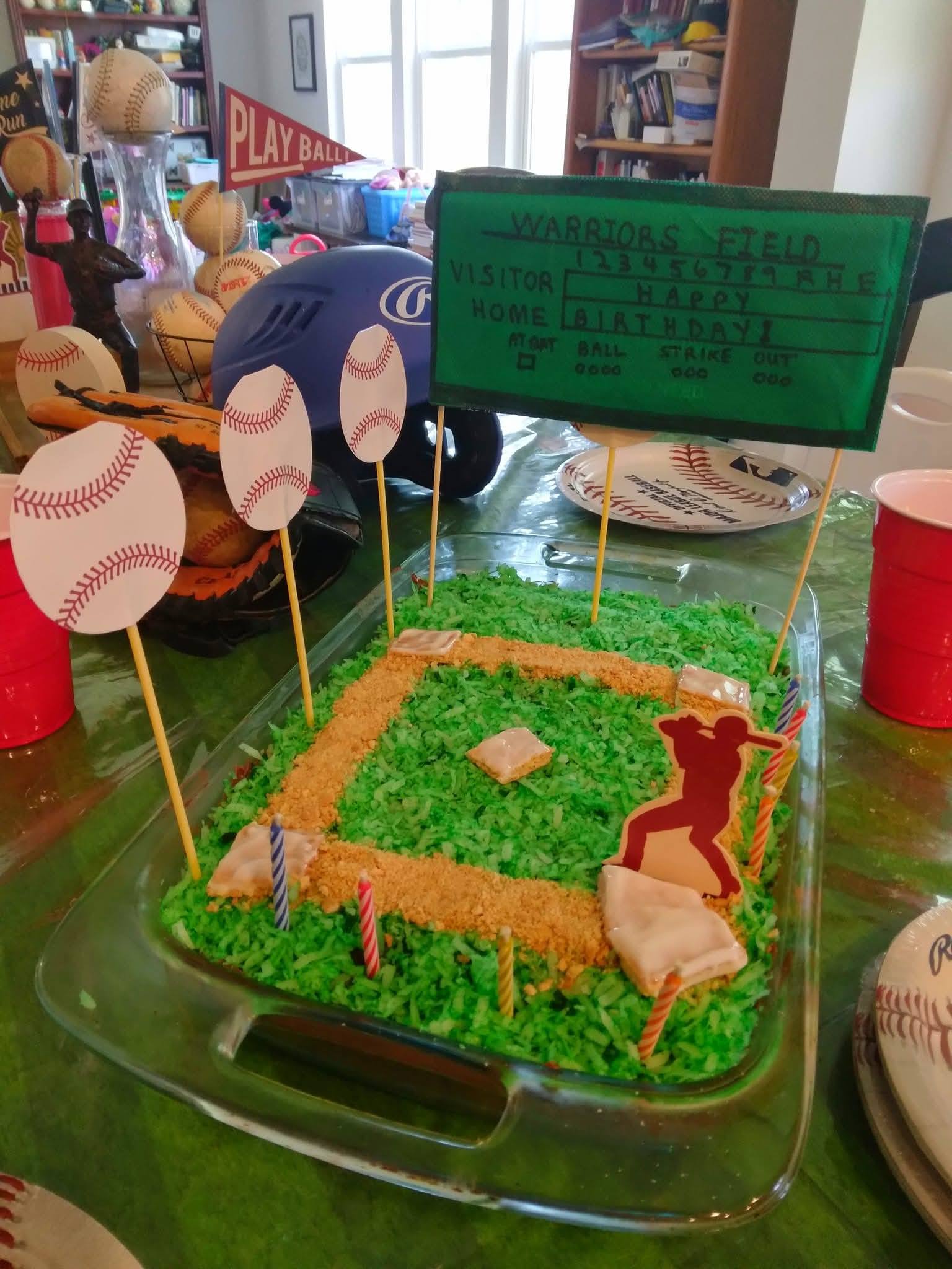 Baseball-themed birthday cake decorated as a baseball field with a scoreboard sign, baseball cutouts, and player.