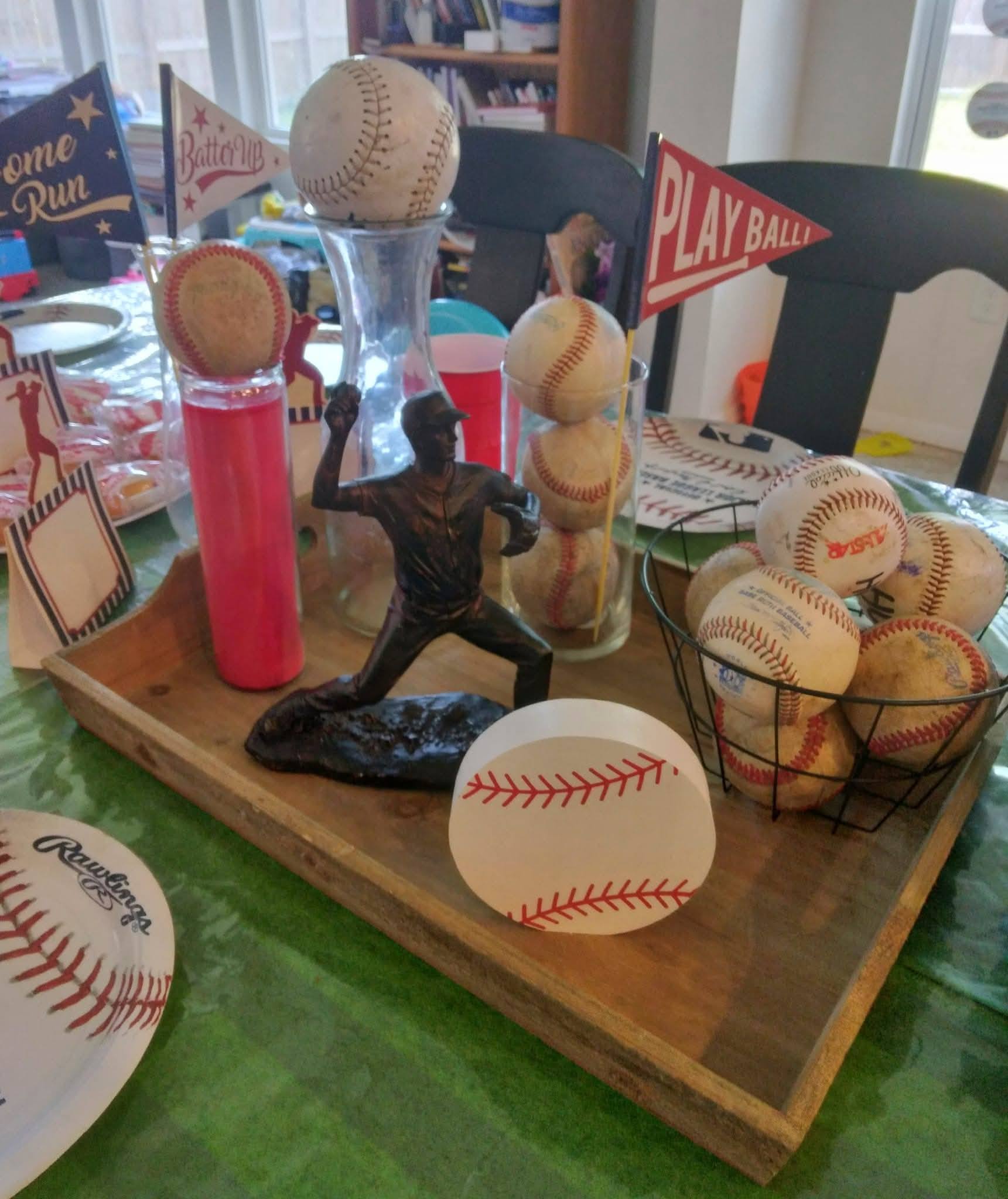 Baseball-themed table centerpiece featuring a bronze pitcher statue, baseballs in glass jars and wire baskets, and miniature pennants.
