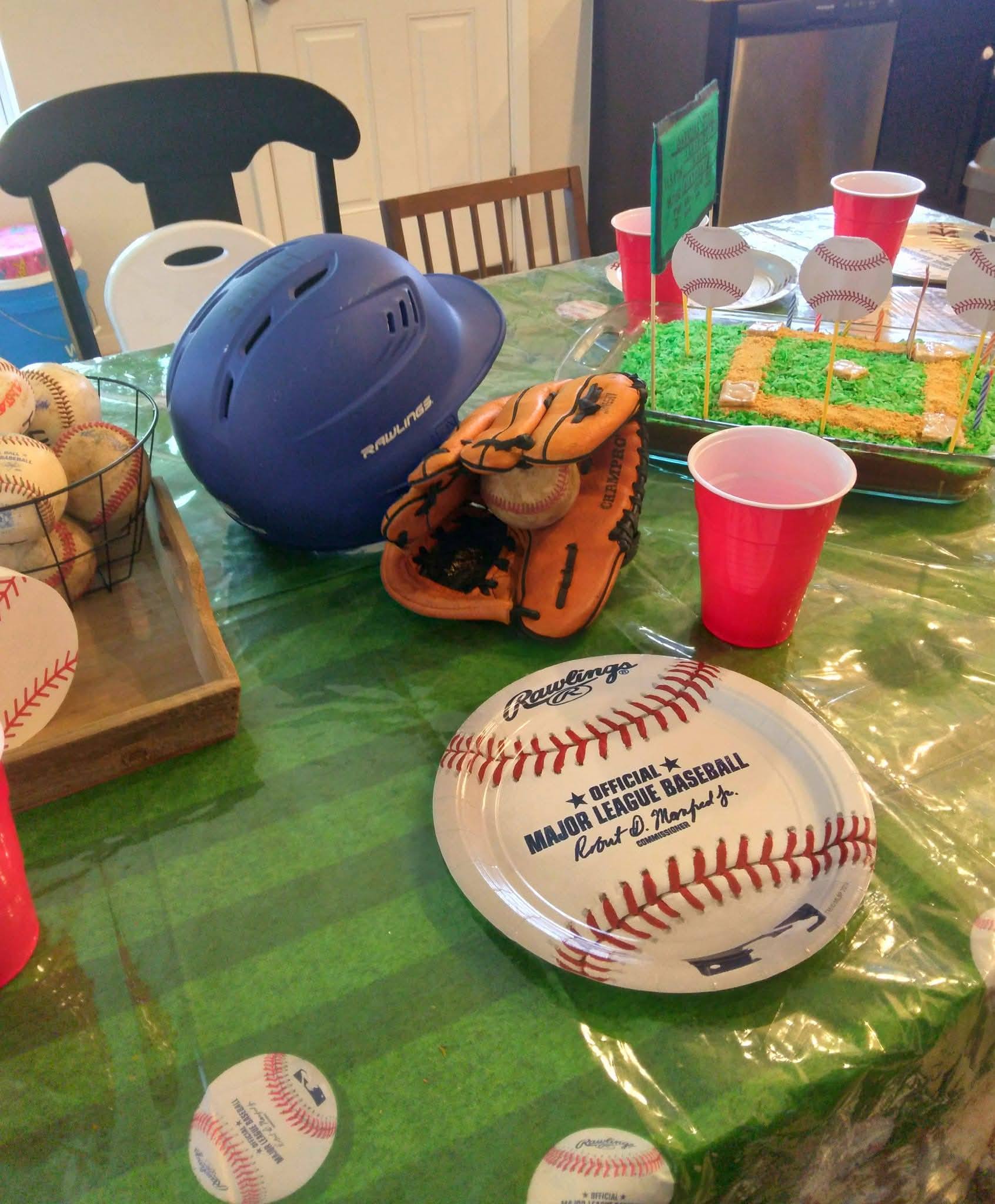 Baseball themed party table with a Rawlings helmet, glove, baseballs, and a baseball field cake.