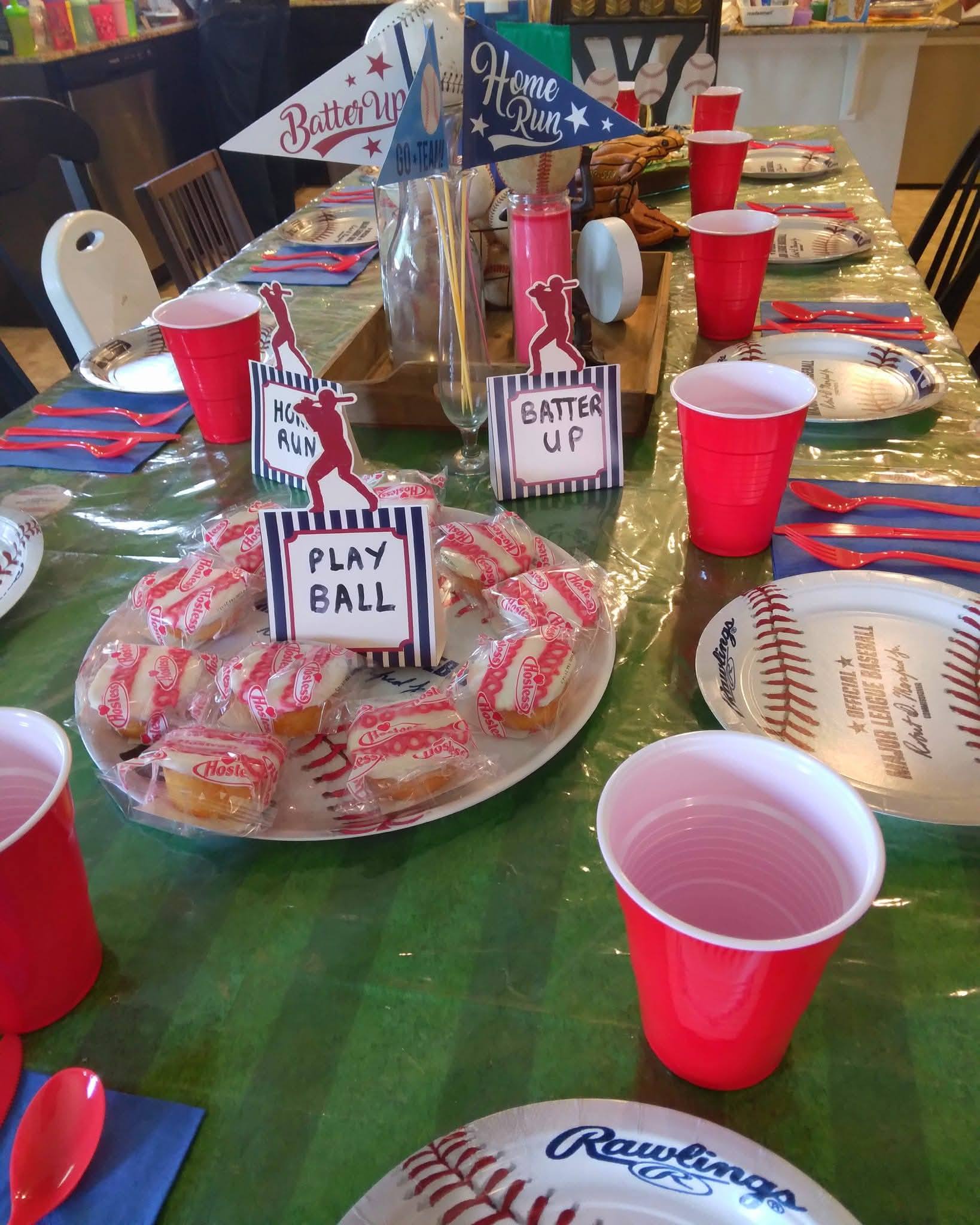 Table set for a baseball-themed party with baseball-patterned plates, red plastic cups, and snack cupcakes.