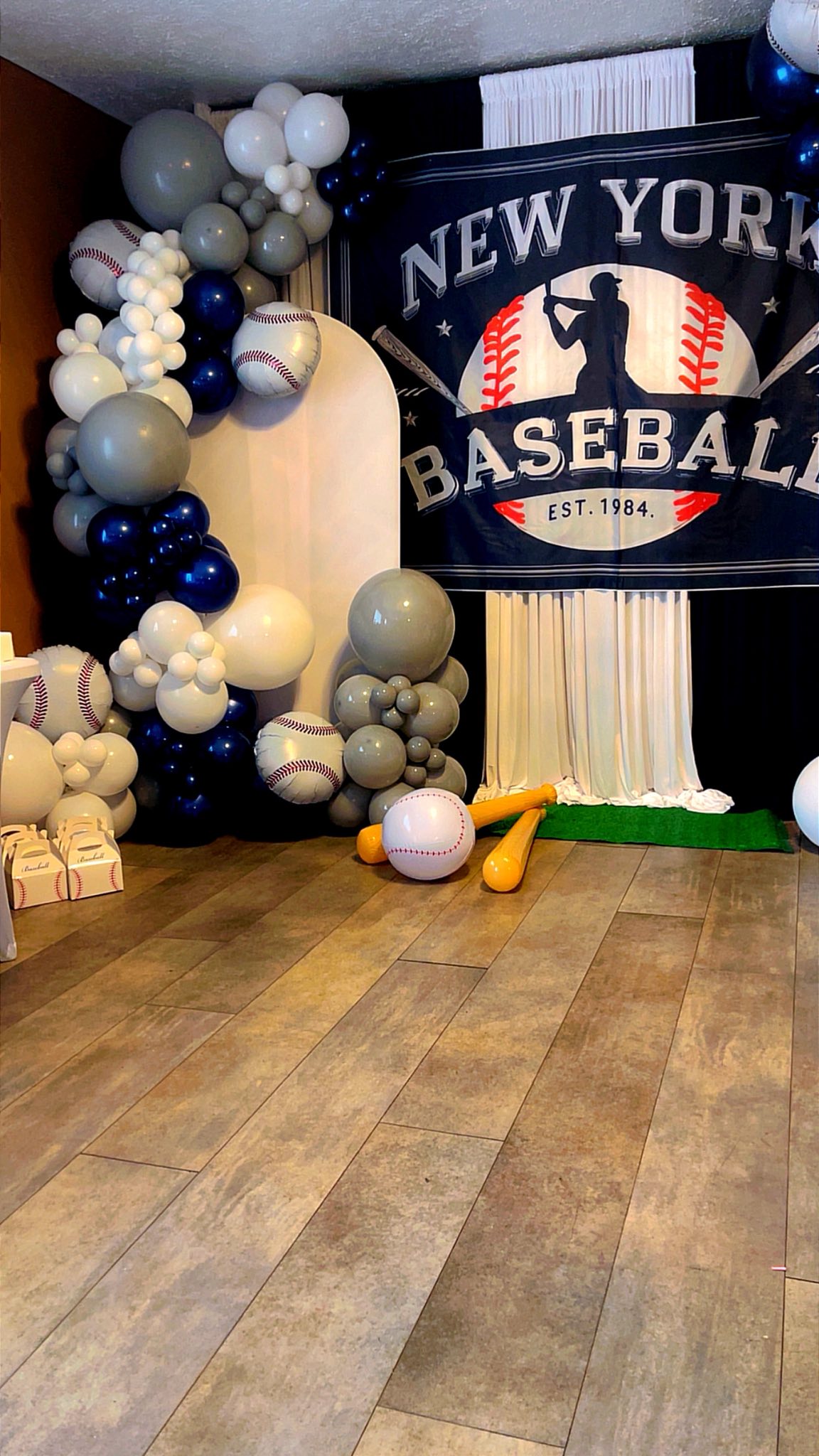 Baseball themed party balloon arch setup with New York Baseball backdrop and inflatable baseball bats.