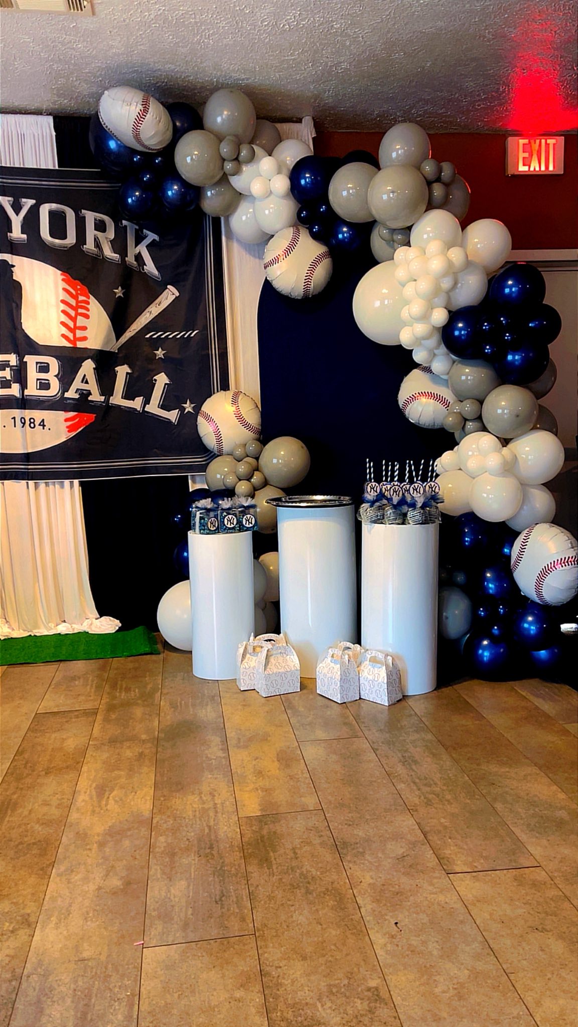 Baseball-themed party backdrop with a balloon arch, party favors, and a New York Yankees banner.