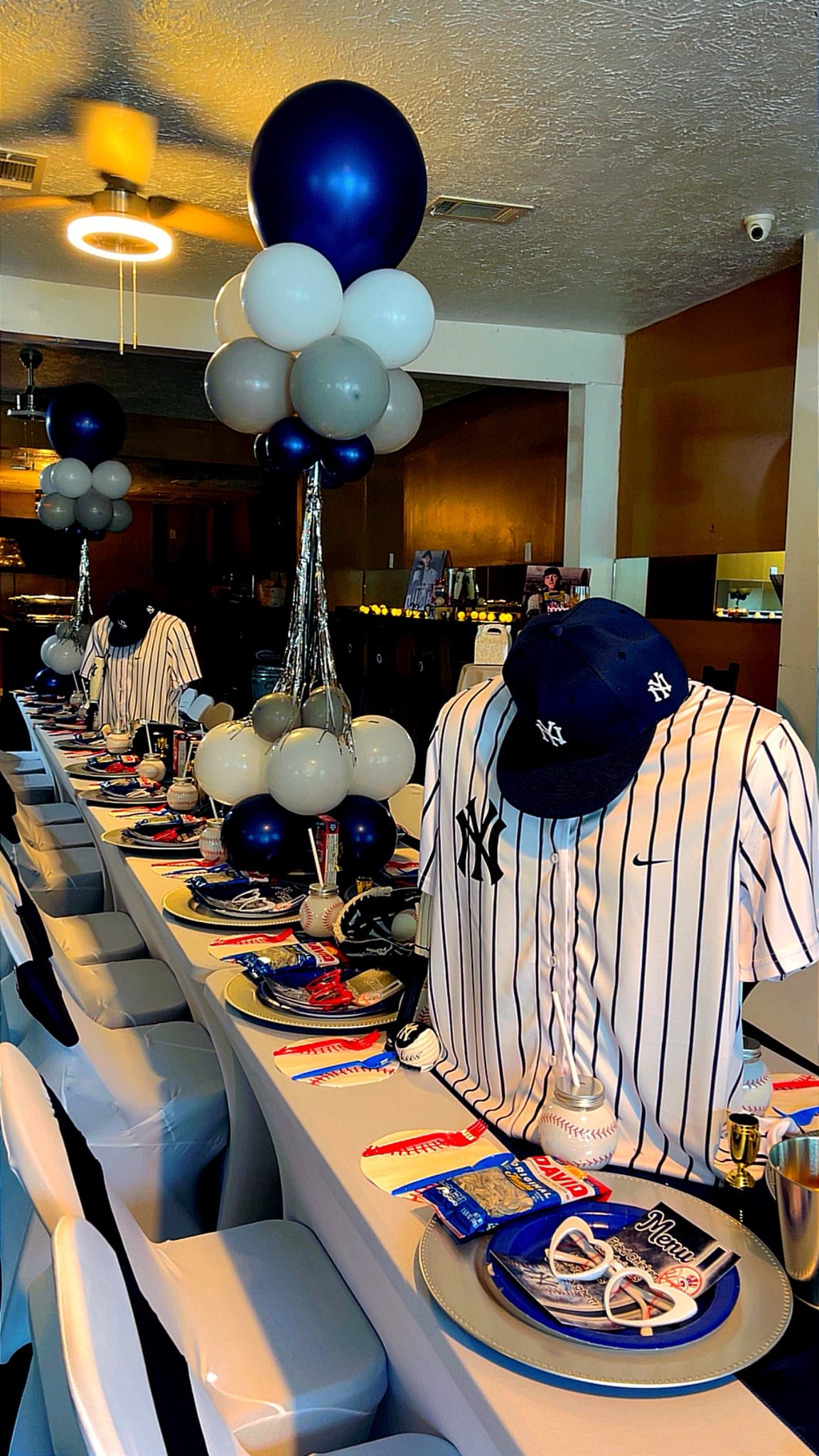Table set for a New York Yankees themed baseball party with team jerseys, hats, and matching balloons.