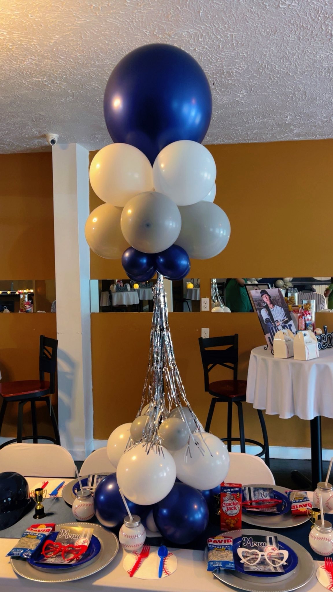 Baseball-themed balloon centerpiece with blue, white, and silver balloons on a decorated party table.