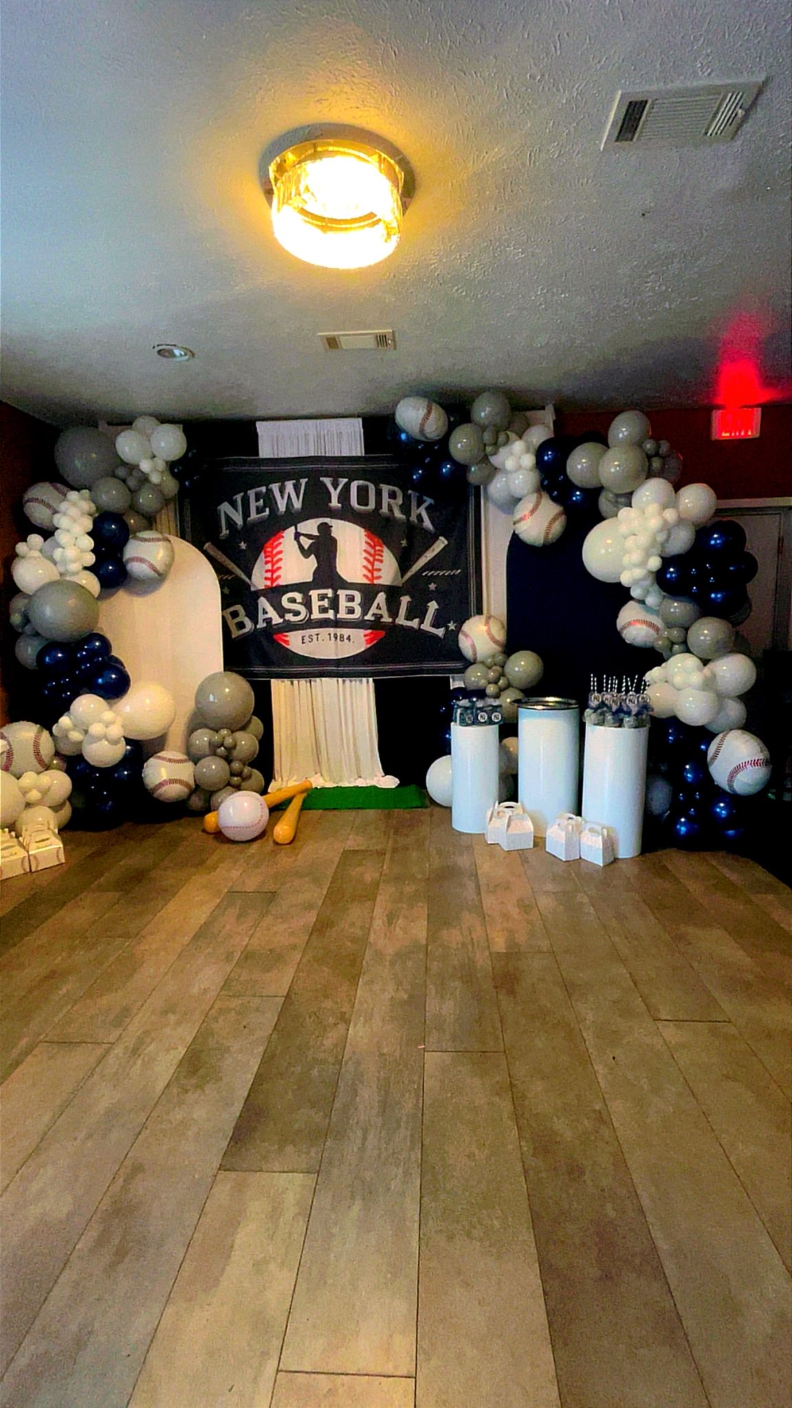 Baseball-themed party backdrop with New York Baseball banner, balloon arch, and white display pedestals.