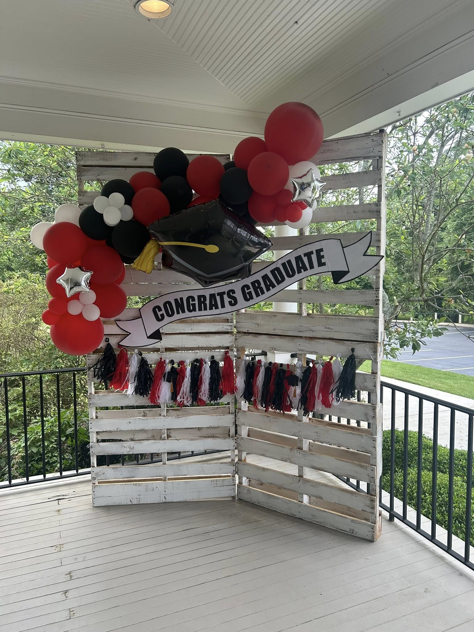 Graduation party backdrop display on a white rustic wooden pallet wall with black, red, and white balloons and a Congratulations Graduate banner.