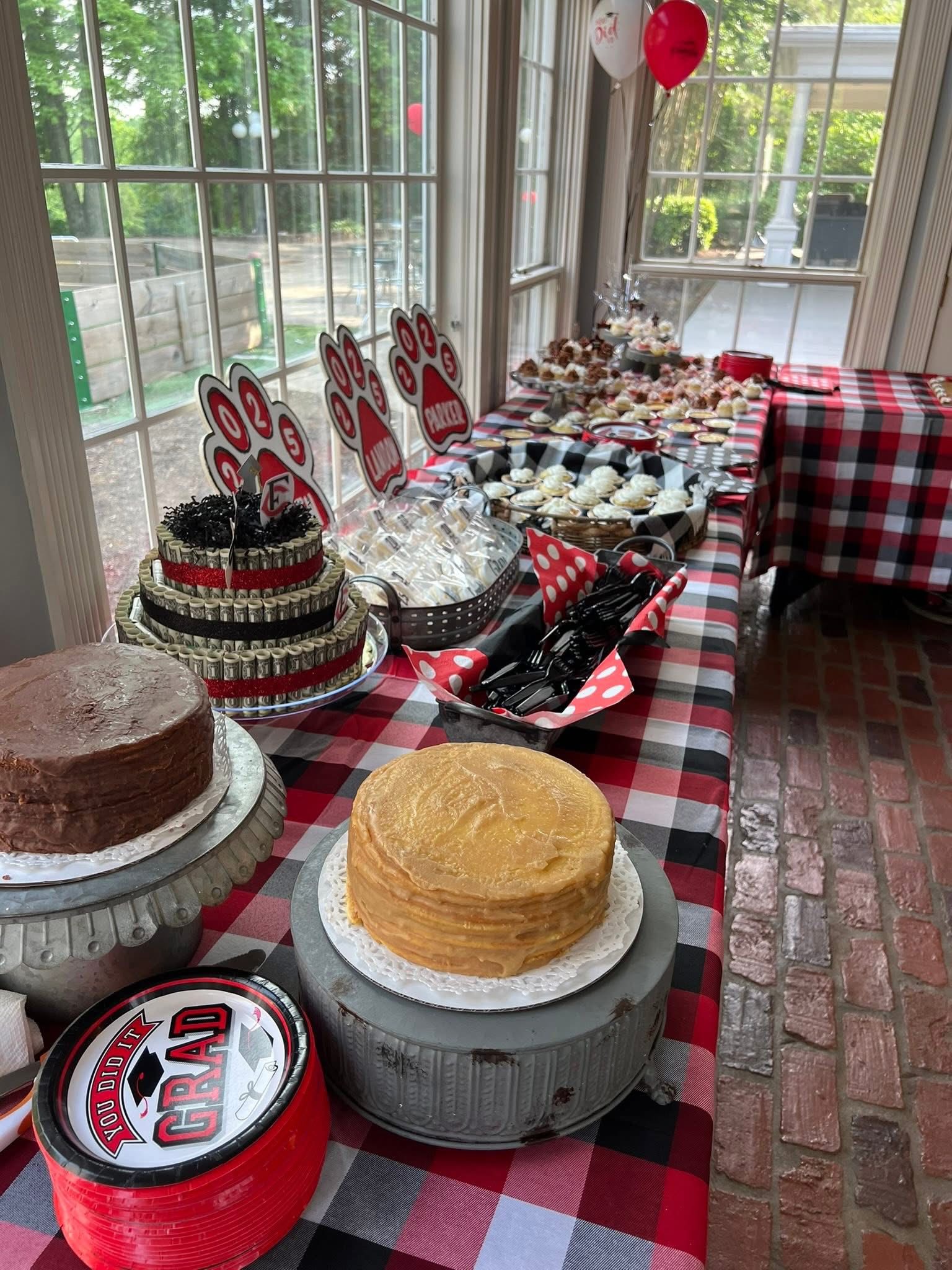 Graduation party dessert table with cakes, cupcakes, and 2025 themed decor on a red and black plaid tablecloth.