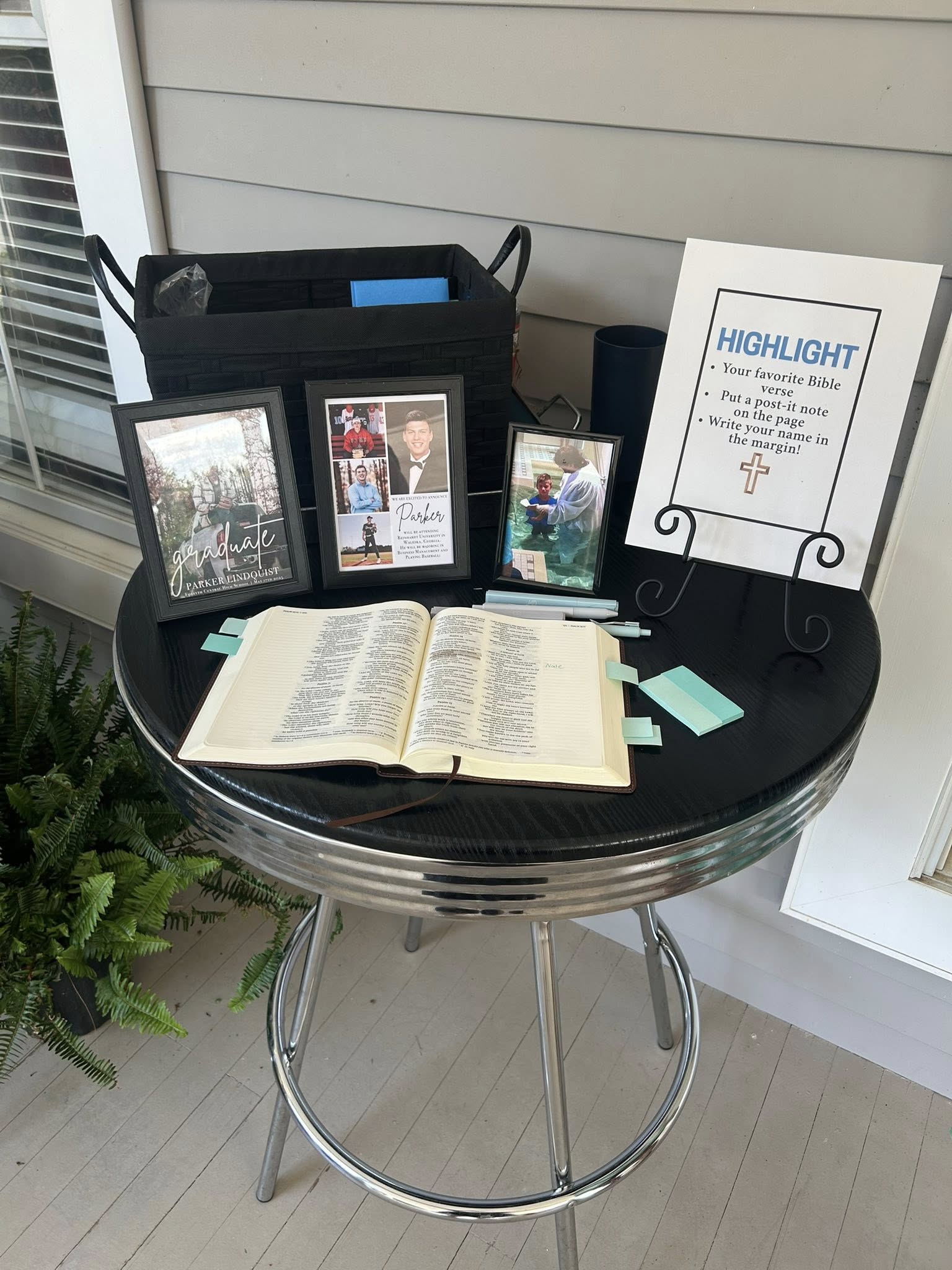 A round table displays a Bible, graduation photos of Parker Lindquist, and a sign inviting guests to highlight a verse.