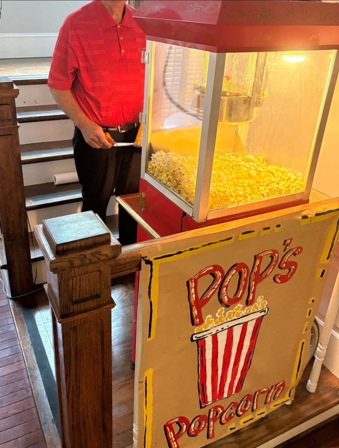 Man standing by a vintage-style popcorn machine with a hand-painted Pop's Popcorn sign.