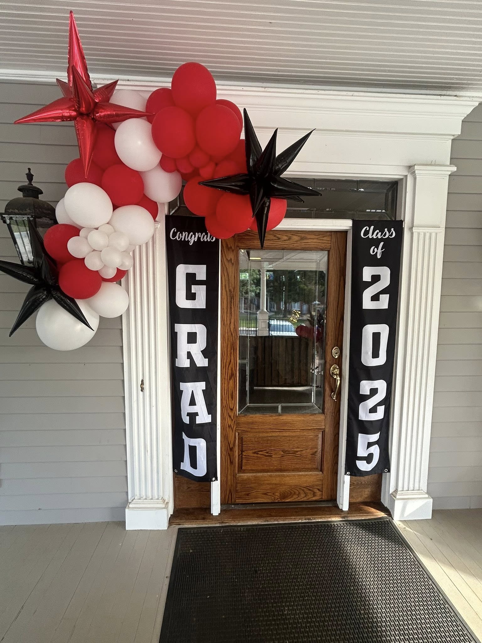 Front door decorated for Class of 2025 graduation with red and white balloon arch and banner.