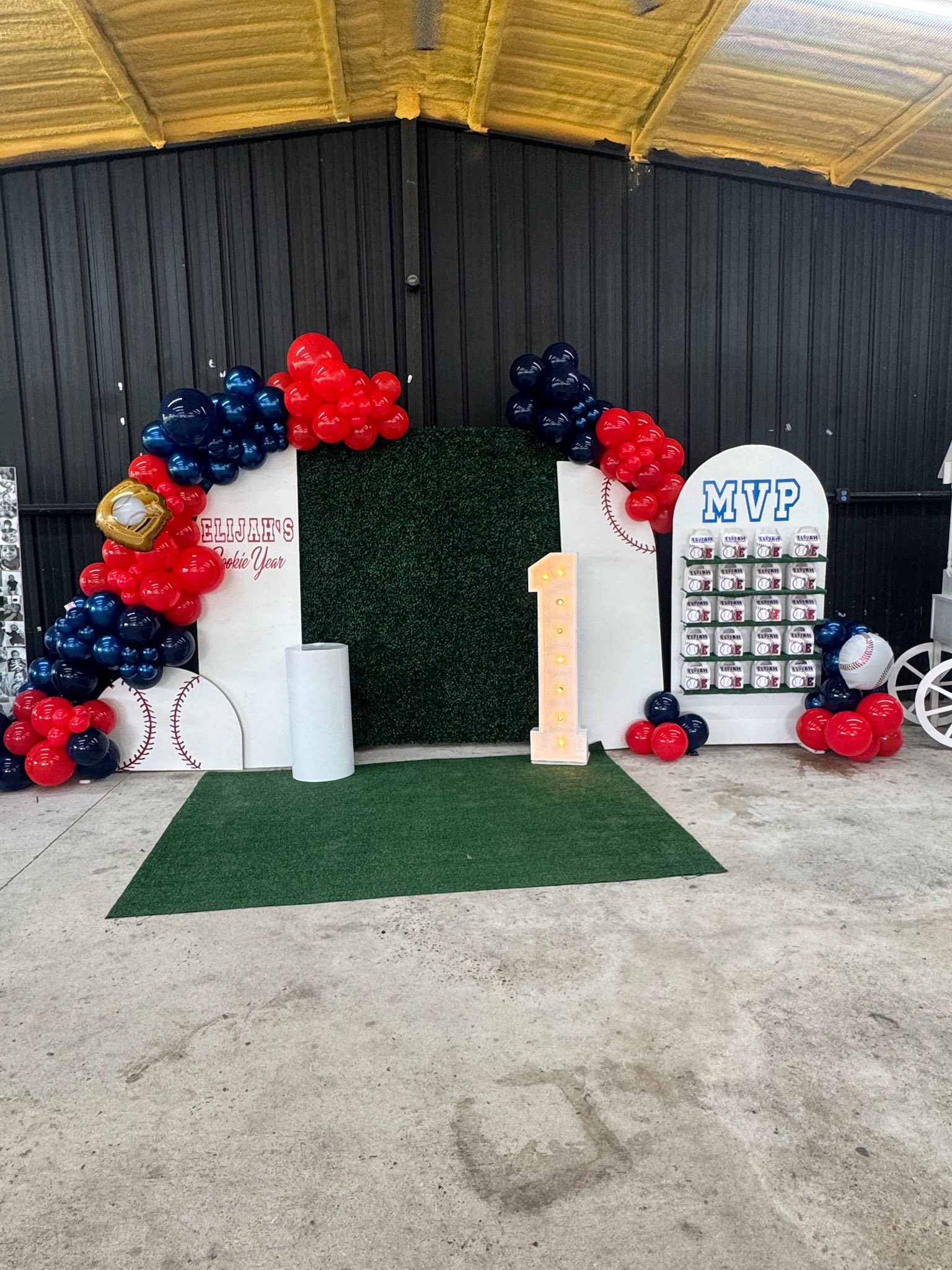 Baseball-themed first birthday party backdrop with red and blue balloons, a light-up number one, and MVP sign.