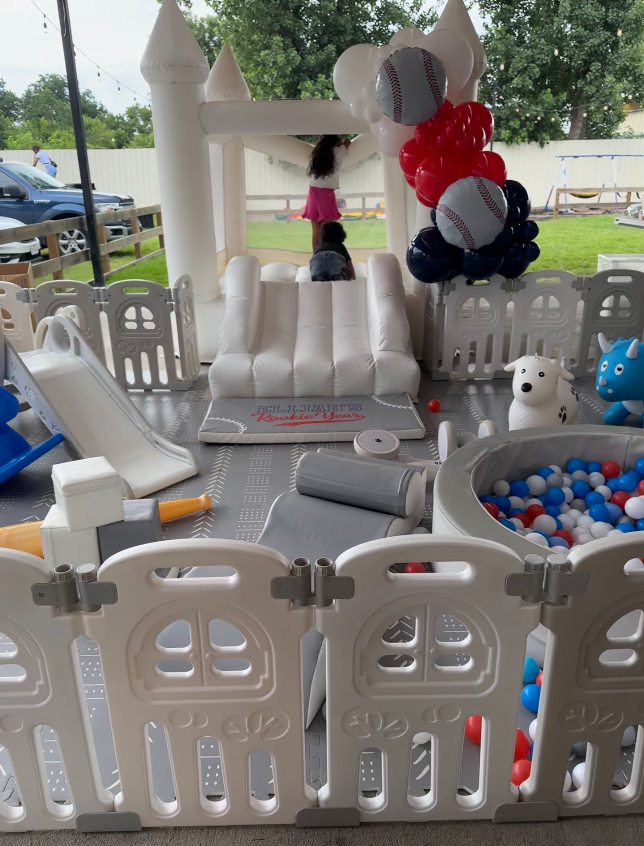 White bounce house setup for a baseball-themed children's party, featuring ball pits, slides, and soft play equipment.