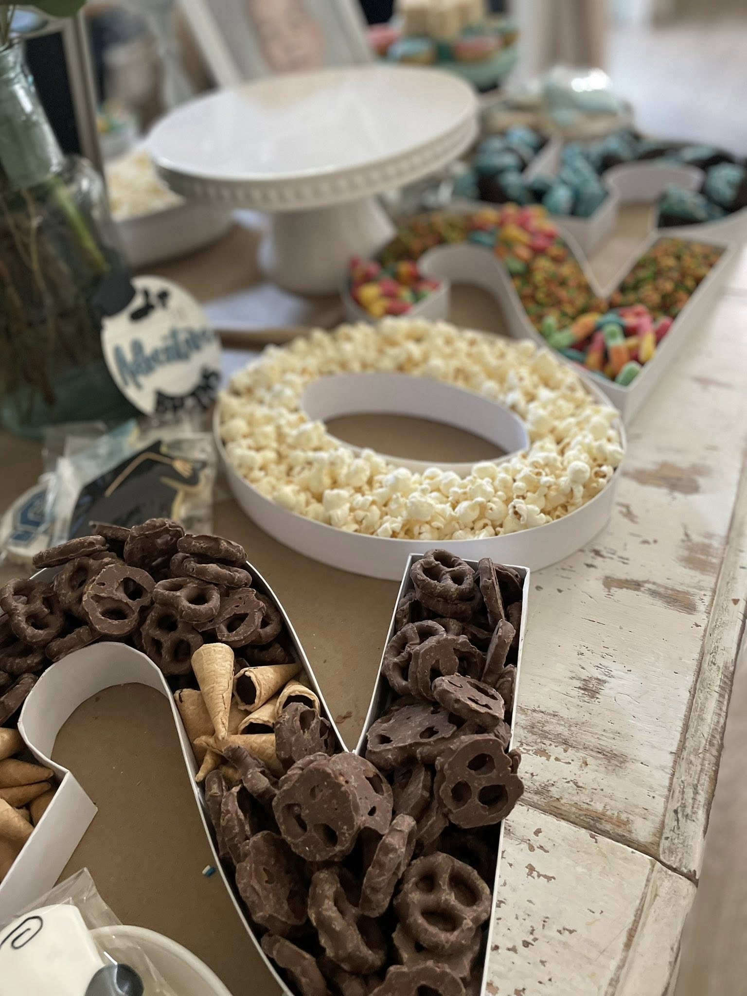 Table filled with letter-shaped snack platters containing popcorn, chocolate-covered pretzels, and candy.