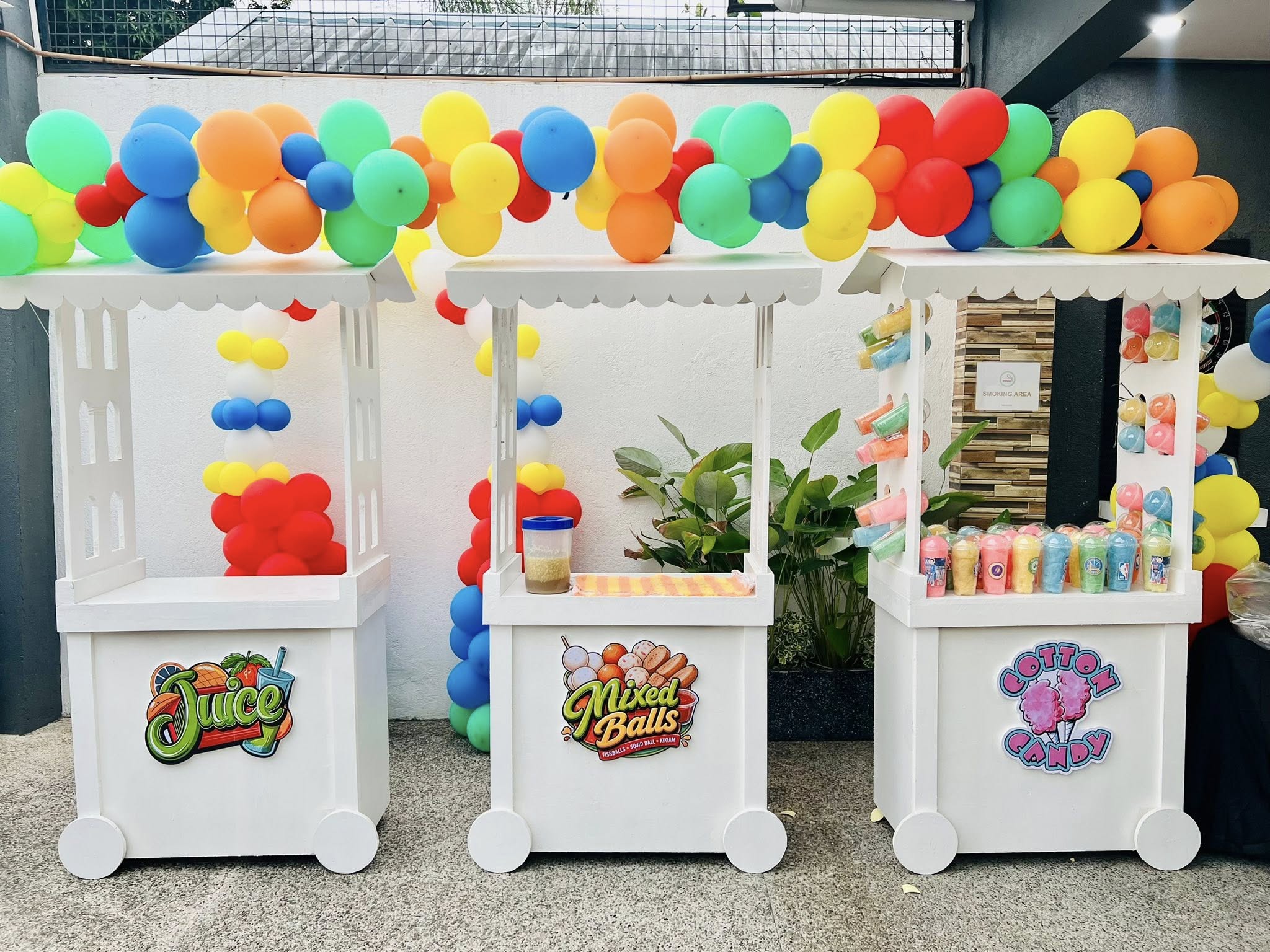 Three decorated party food carts featuring Juice, Mixed Balls, and Cotton Candy, surrounded by balloon arches.