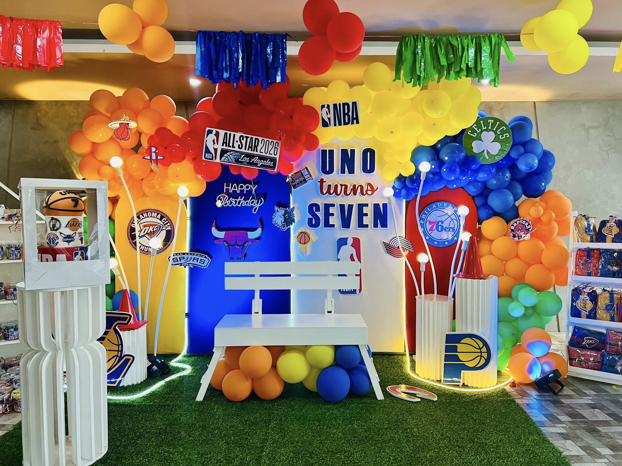 Birthday party photo backdrop with NBA themed balloon arches, basketball logos, and bench seating.