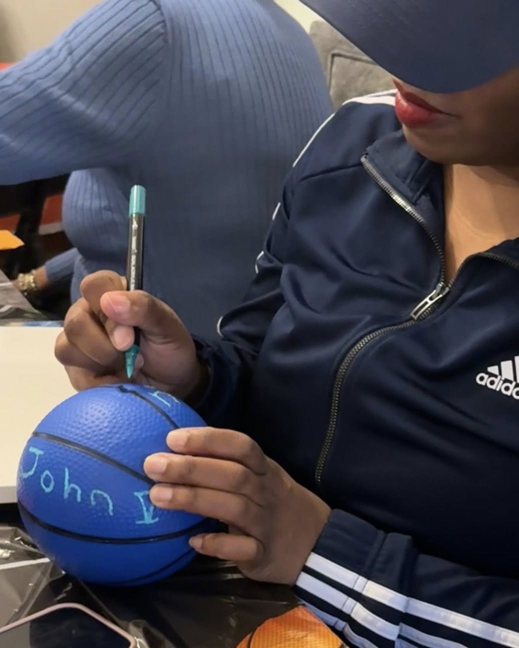 Person signing the name John onto a small blue toy basketball with a marker.