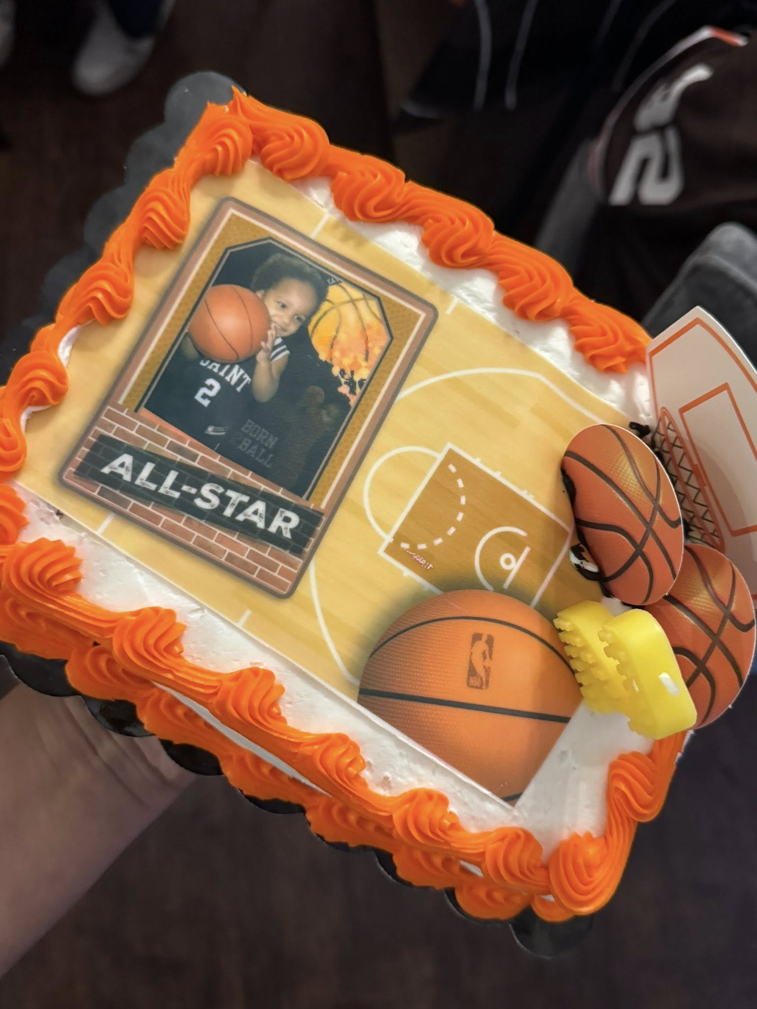Rectangular basketball-themed sheet cake with orange frosting, basketball court edible image, and basketball toppers.