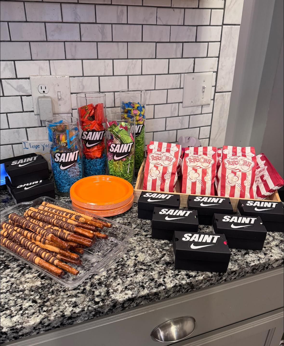 Party snack station featuring chocolate-dipped pretzel rods, striped popcorn bags, and custom Saint favor boxes.