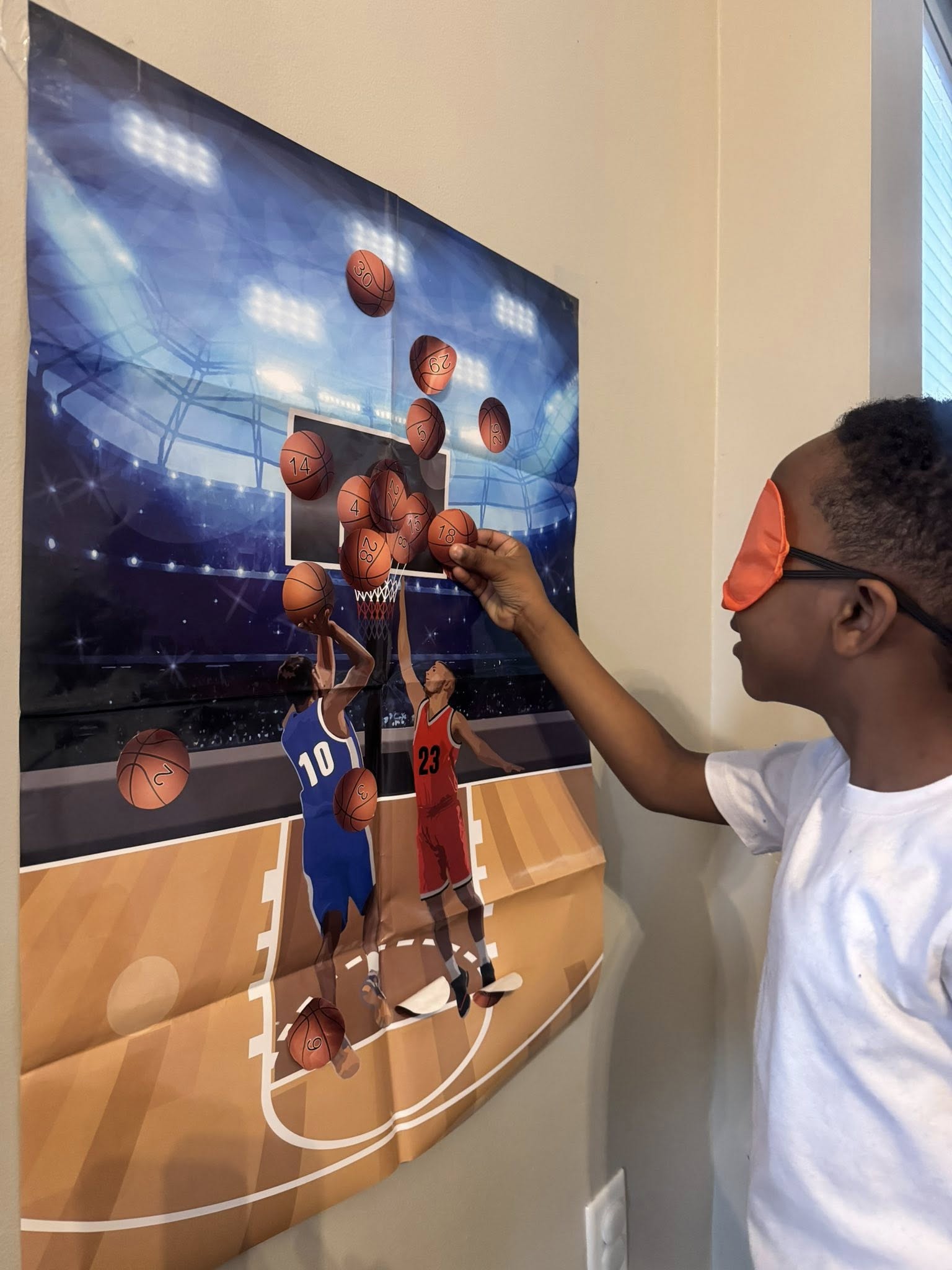 Child playing basketball pin the ball game wearing an orange blindfold
