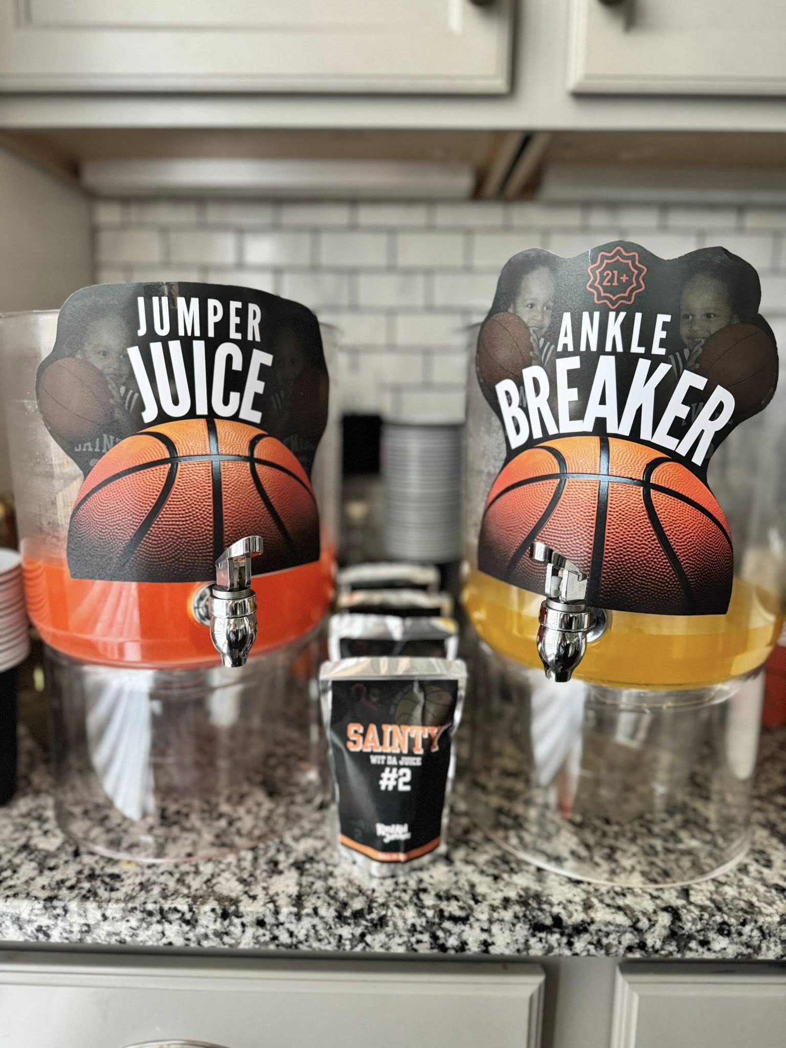 Two beverage dispensers labeled Jumper Juice and Ankle Breaker with basketball designs, next to a Sainty #2 drink bag.