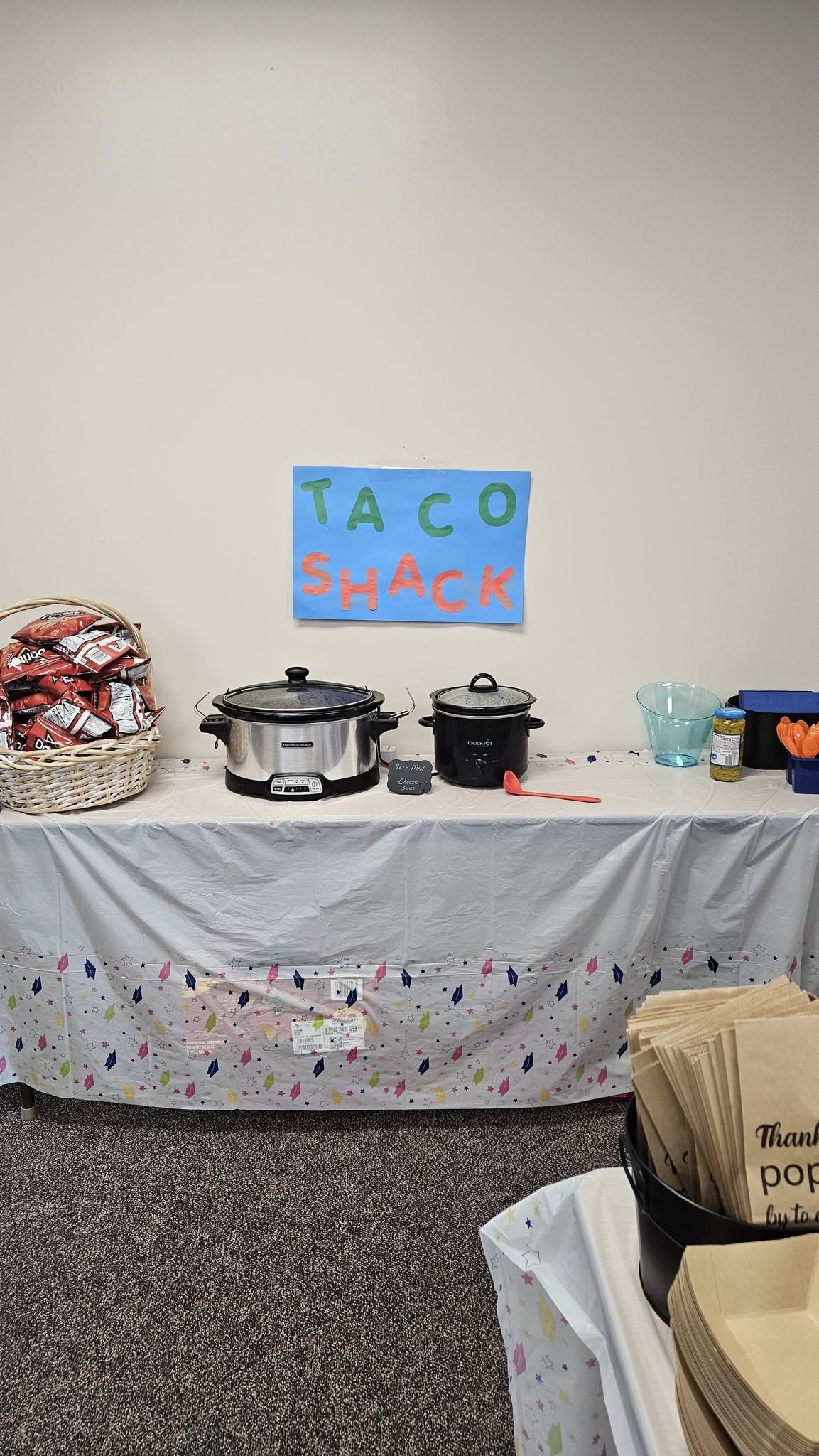 Taco Shack buffet table with slow cookers, a basket of chips, and paper serving bags.