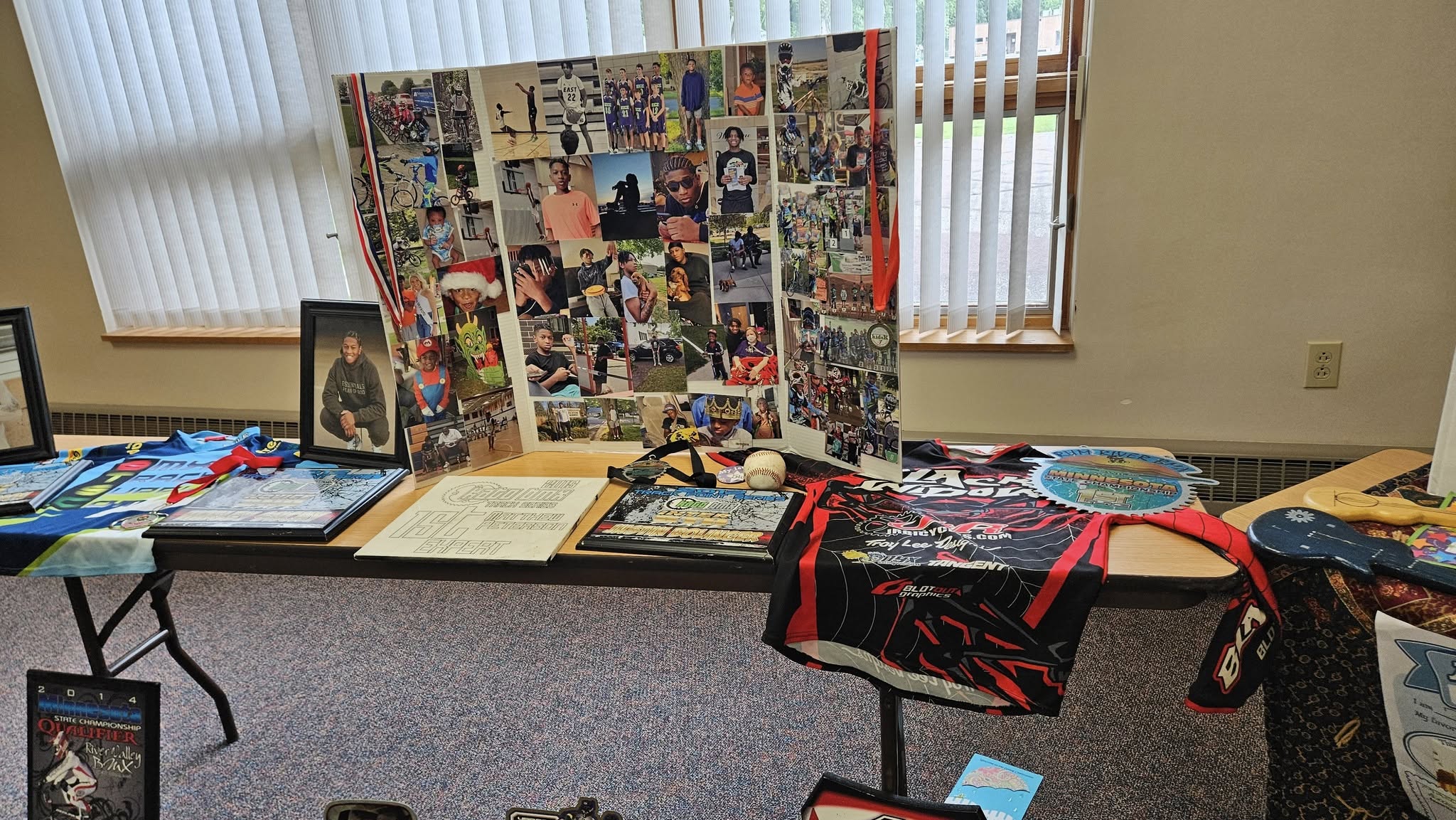 Memorial table with a photo collage, racing jersey, and awards commemorating a BMX enthusiast.