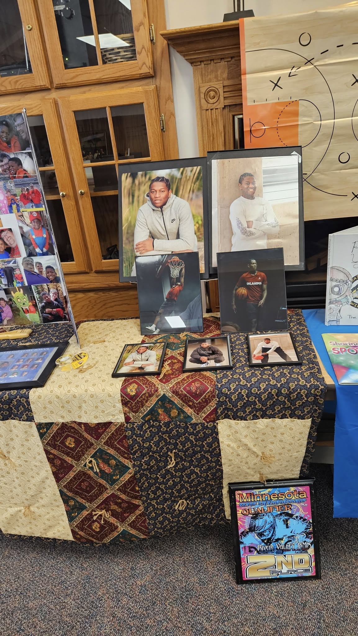Table display featuring various portrait and basketball action photos of a young athlete alongside a BMX trophy.