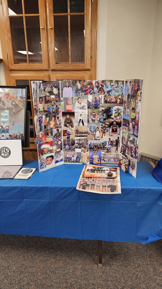 Table display featuring a photo collage board of student athletes, basketball team pictures, and graduation materials.