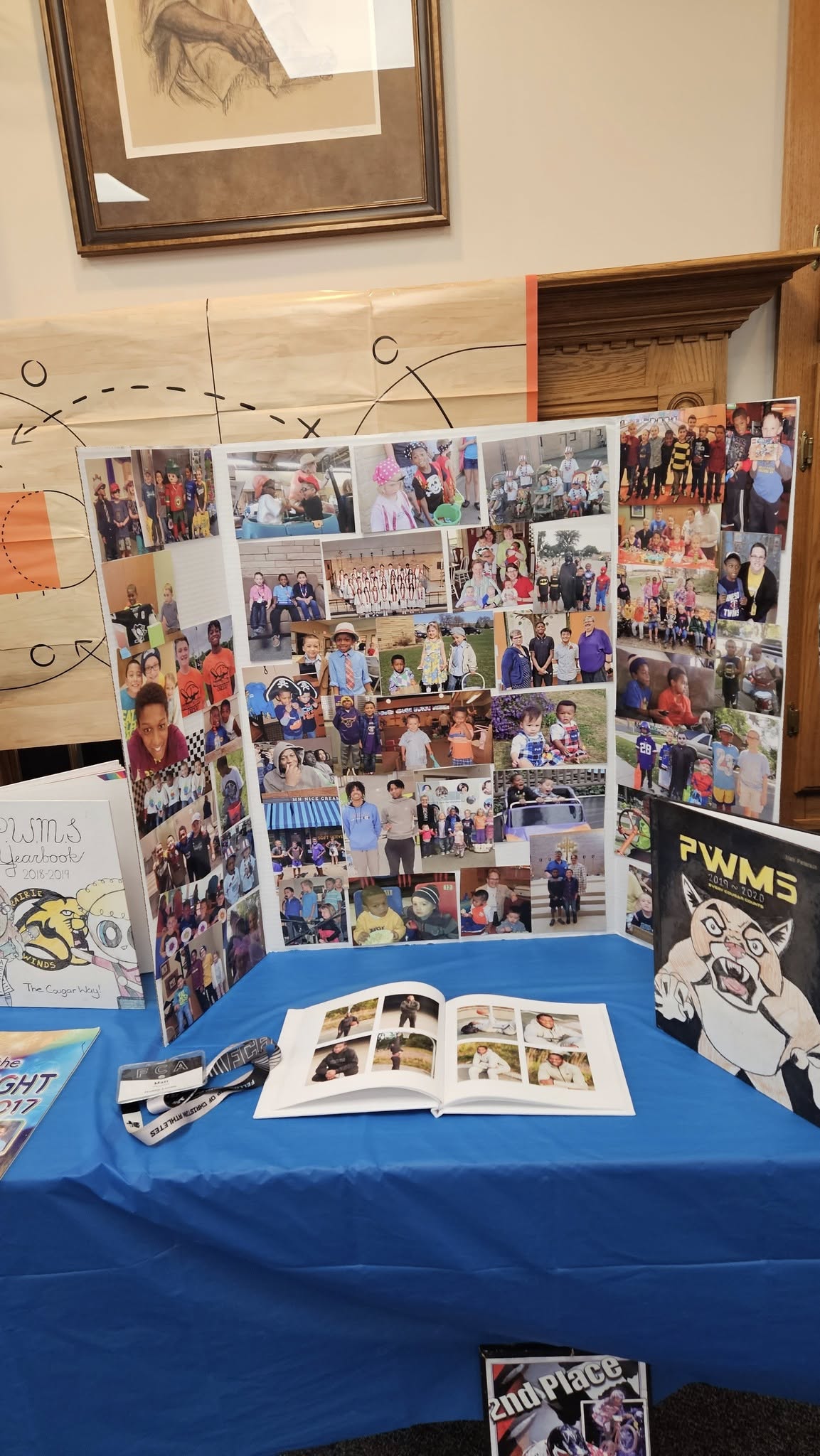 Display board featuring a collage of student photos, school yearbooks, and memorabilia on a blue tablecloth.