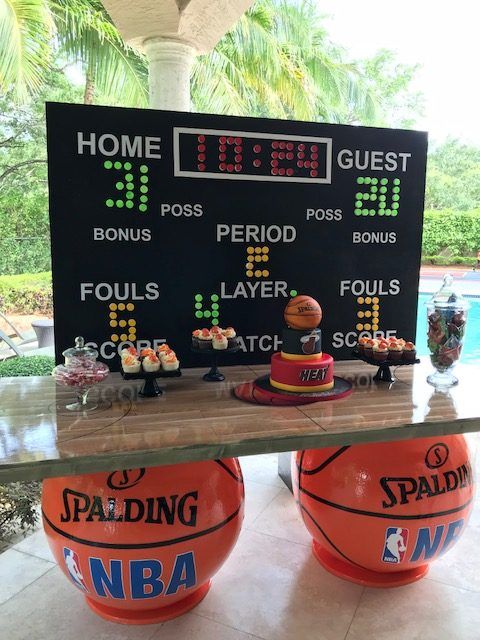 Basketball-themed party dessert table with a scoreboard backdrop, Miami Heat birthday cake, and basketball base stands
