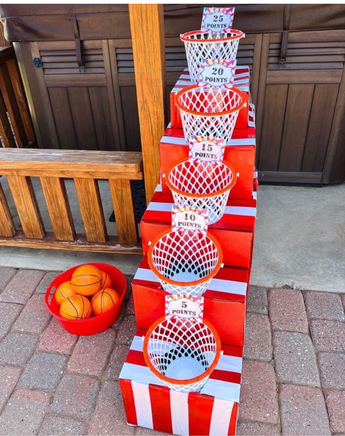 Carnival-style basketball toss game with tiered point baskets and small basketballs in a red bin.