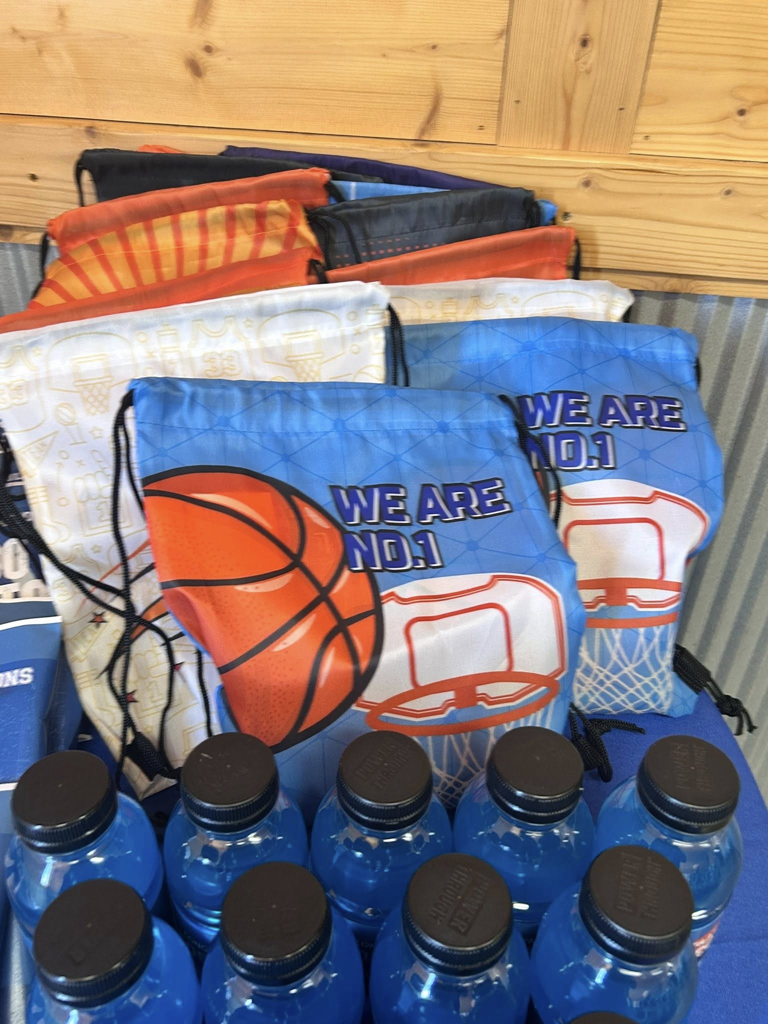 Stack of basketball themed drawstring bags with We Are No. 1 text and blue sports drinks in front