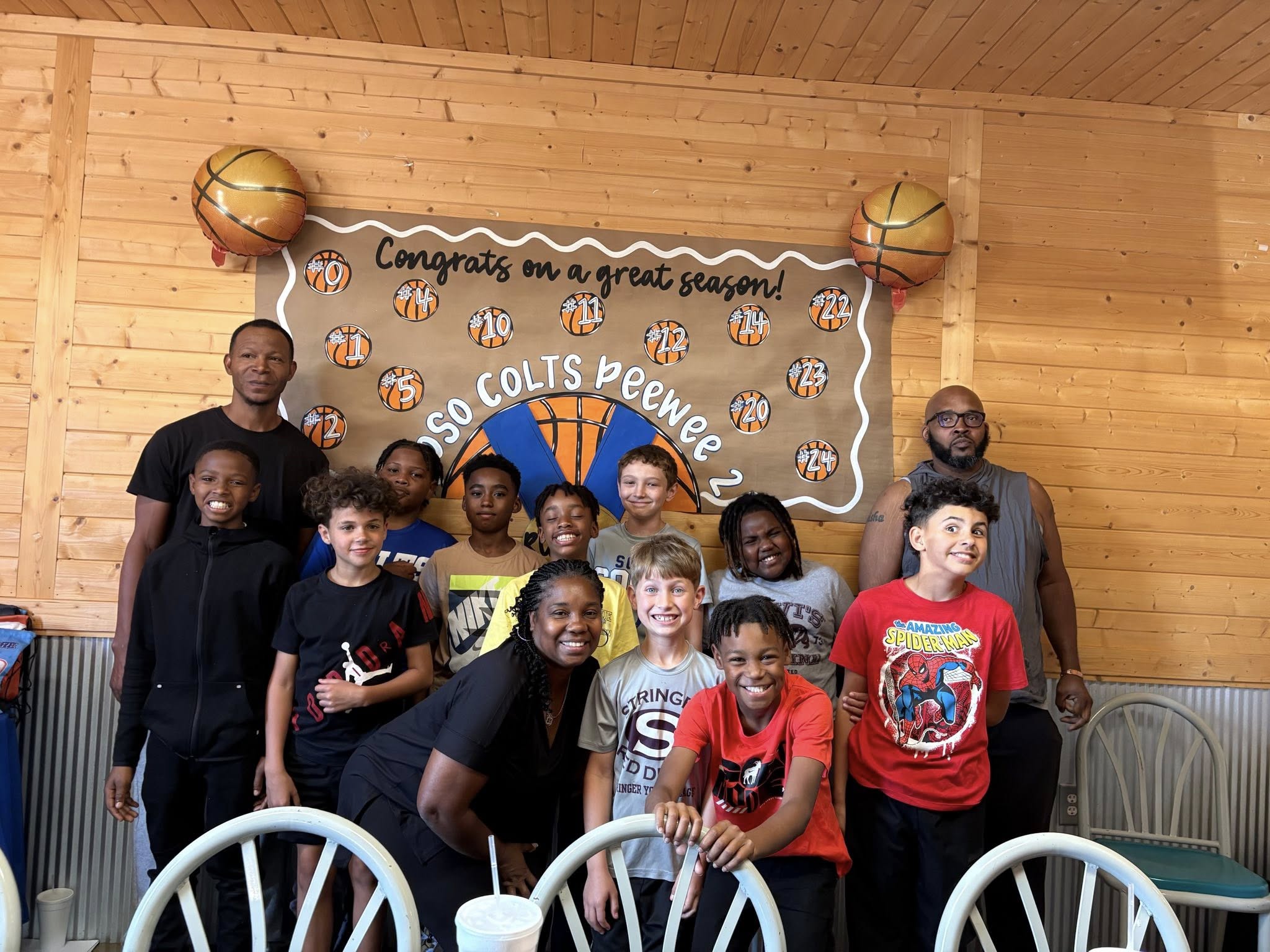 Group of young basketball players and coaches posing in front of a celebratory season poster