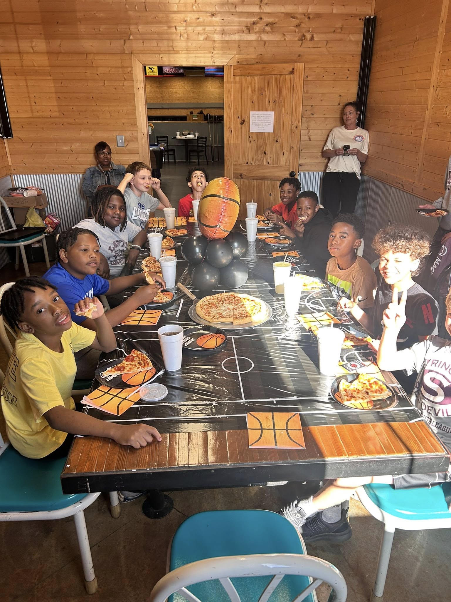 Group of children at a basketball-themed birthday party eating pizza at a long table.