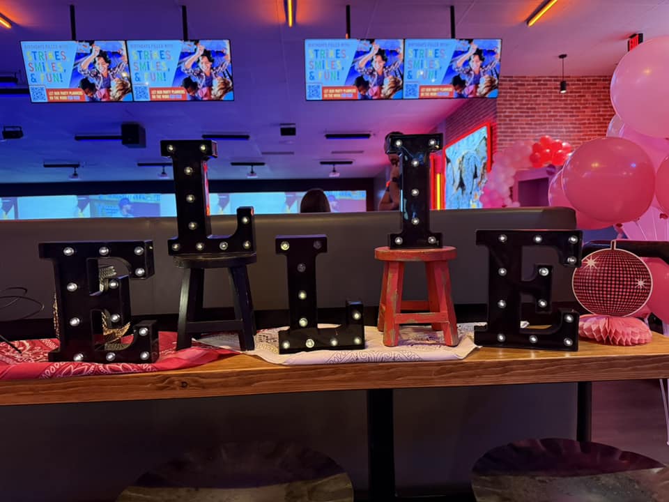 Light-up marquee letters spelling Ellie on a bowling alley party table.