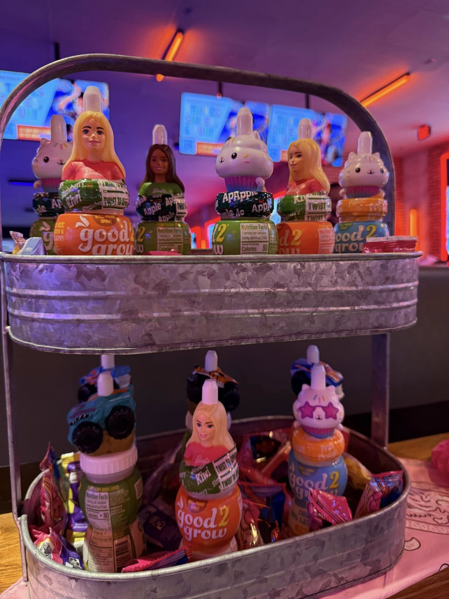 Two-tiered galvanized metal tray filled with Good2Grow juice bottles featuring collectible toy toppers.