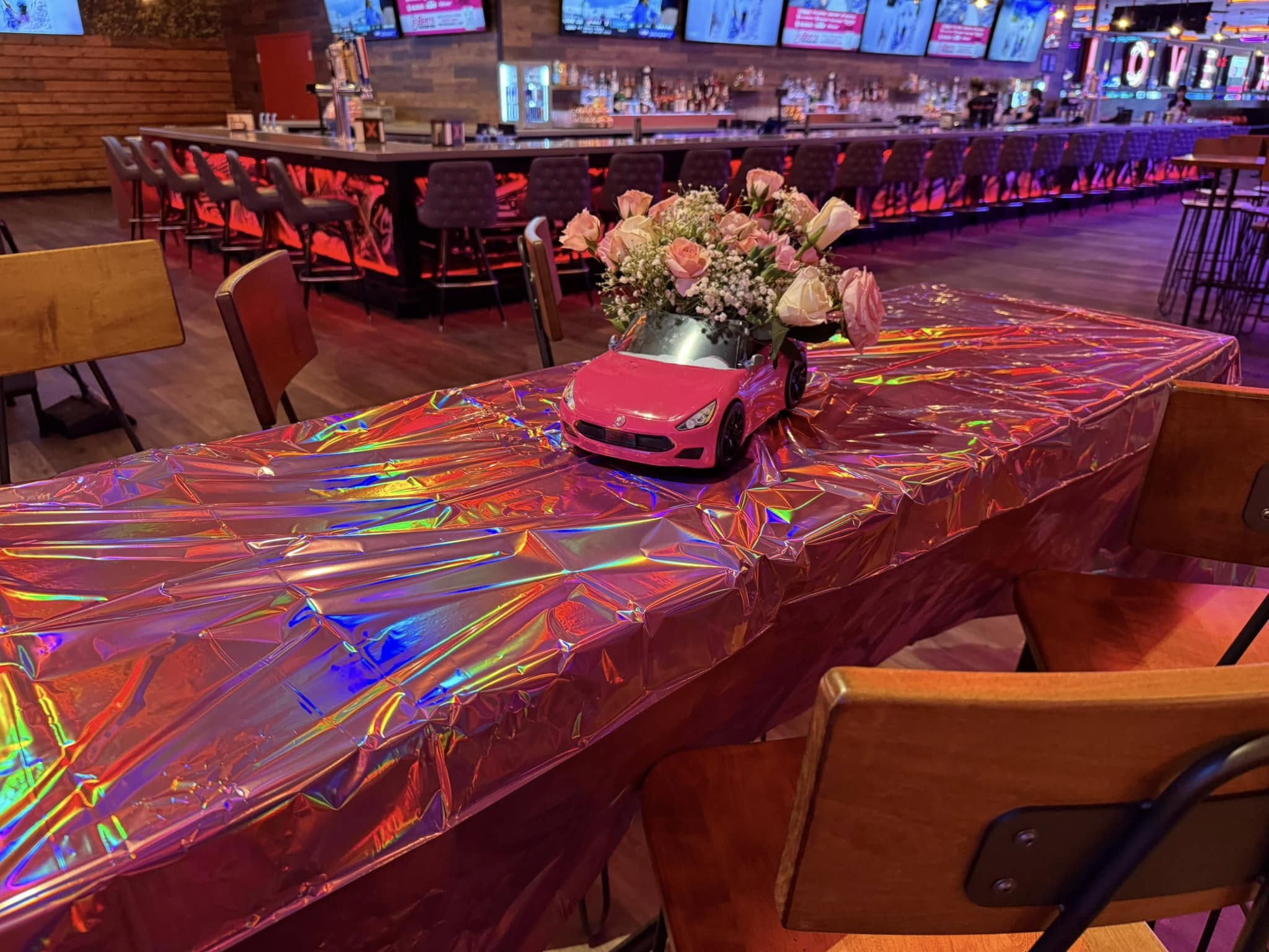 Table centerpiece featuring a miniature pink car filled with pink and white roses inside a restaurant.