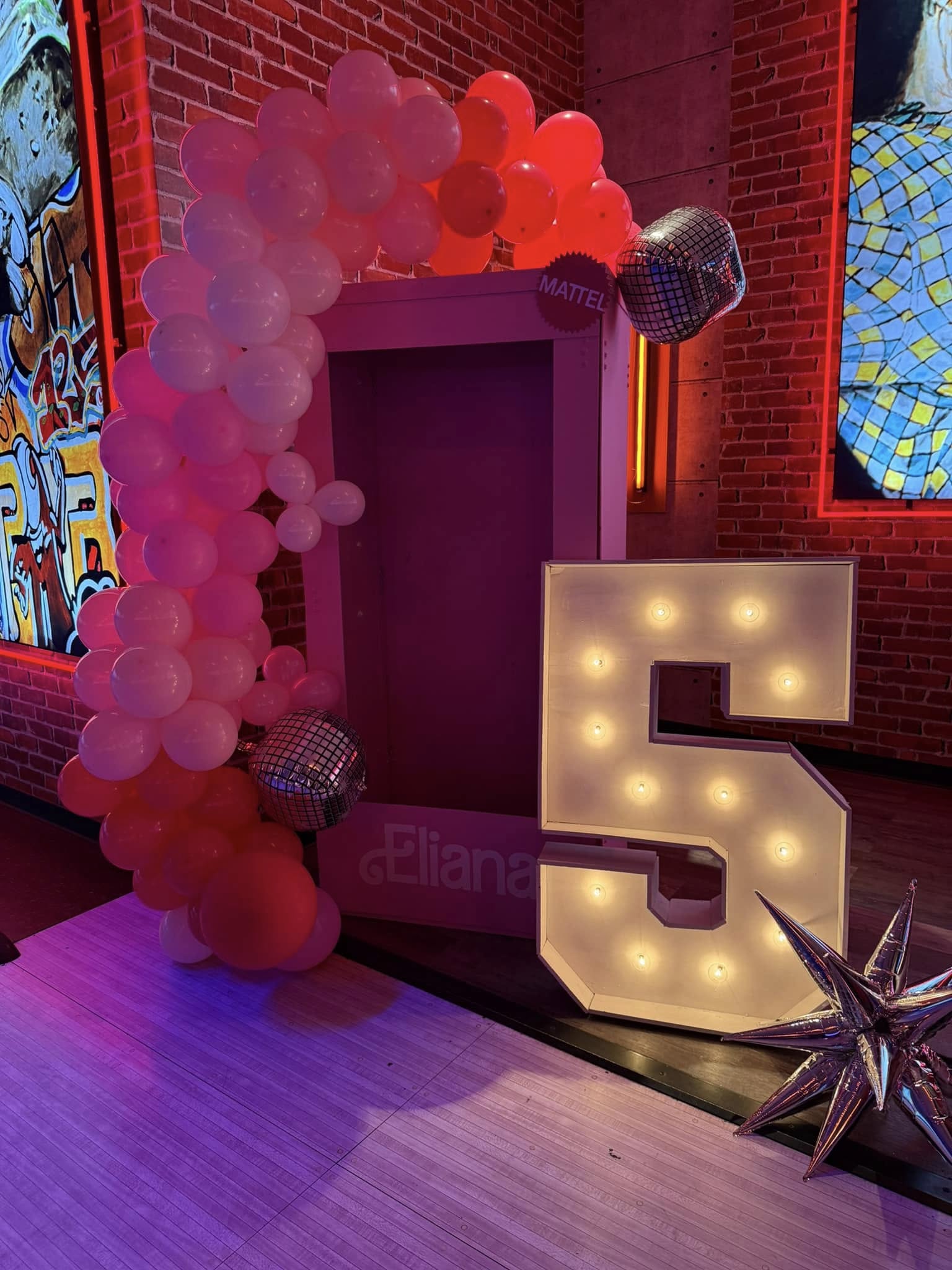 Life-sized Barbie-style doll box for a birthday party with a pink balloon arch and a large lighted number five.