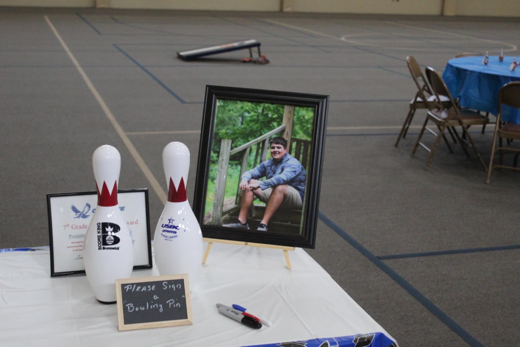Table with two bowling pins for guests to sign, a framed portrait of a young man, and a commemorative award.