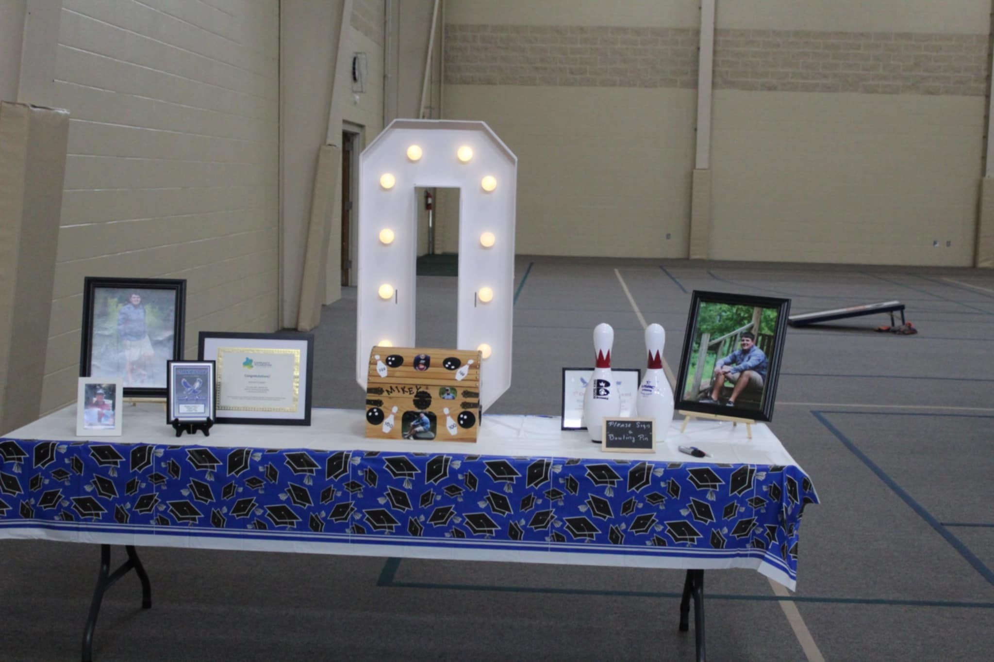 Graduation party head table with light-up number decoration, photos of the graduate, and custom bowling pins.