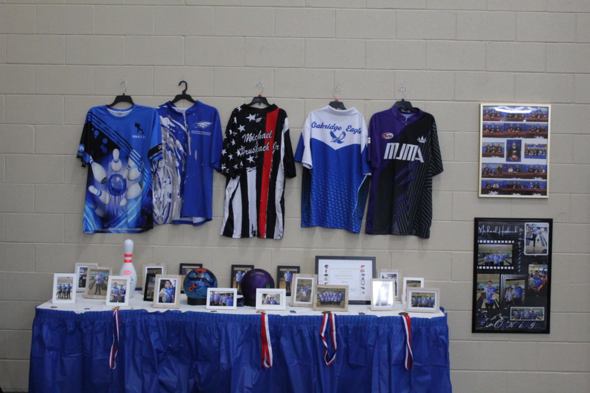 Memorial display table with bowling jerseys, photos, and bowling balls honoring Michael Hruskach Jr.