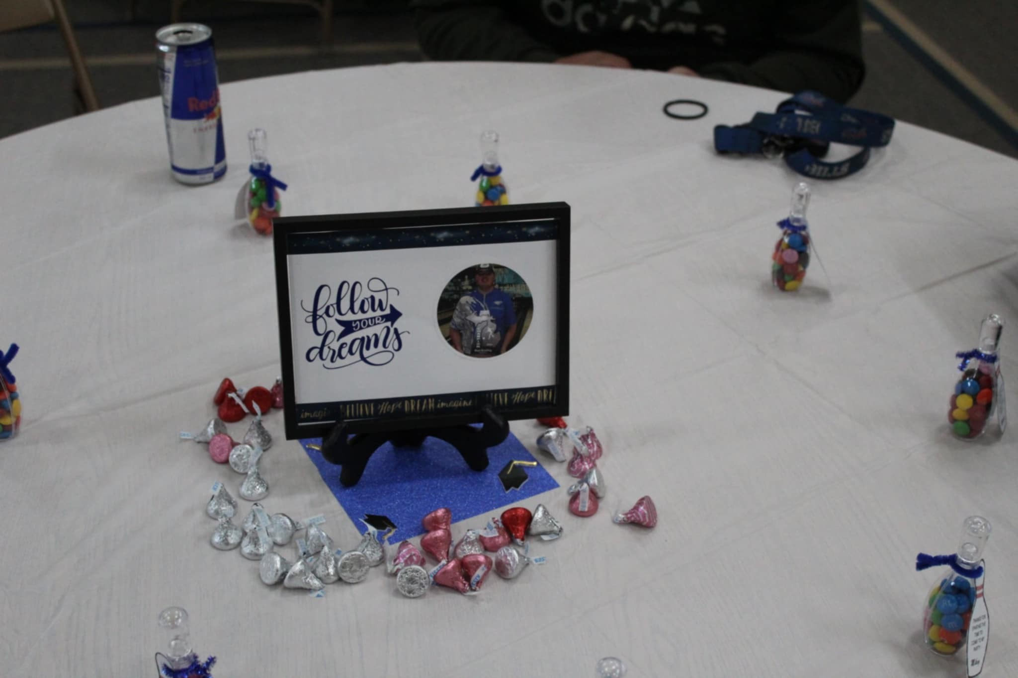 Framed photo with text Follow Your Dreams surrounded by Hershey Kisses and candy-filled bowling pin favors on a table