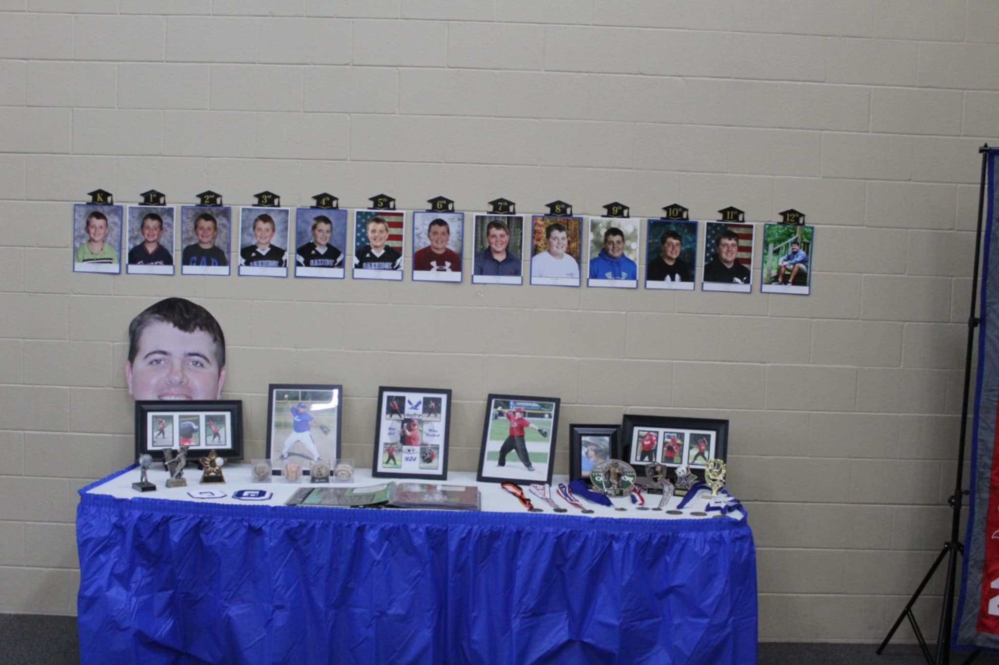 Display table featuring baseball awards, photographs of a student over the years, and a paper cutout head