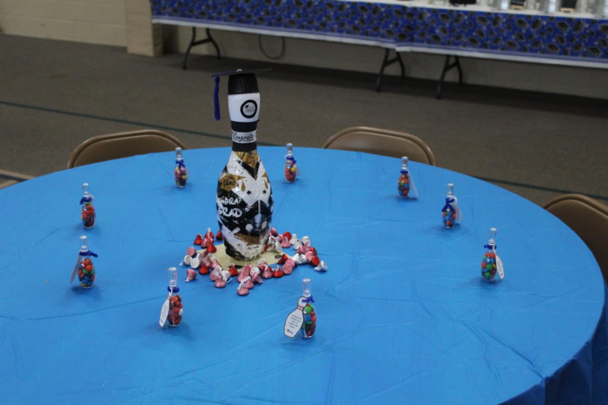 Bowling pin graduation 2023 centerpiece surrounded by candy-filled small bottles on a blue tablecloth