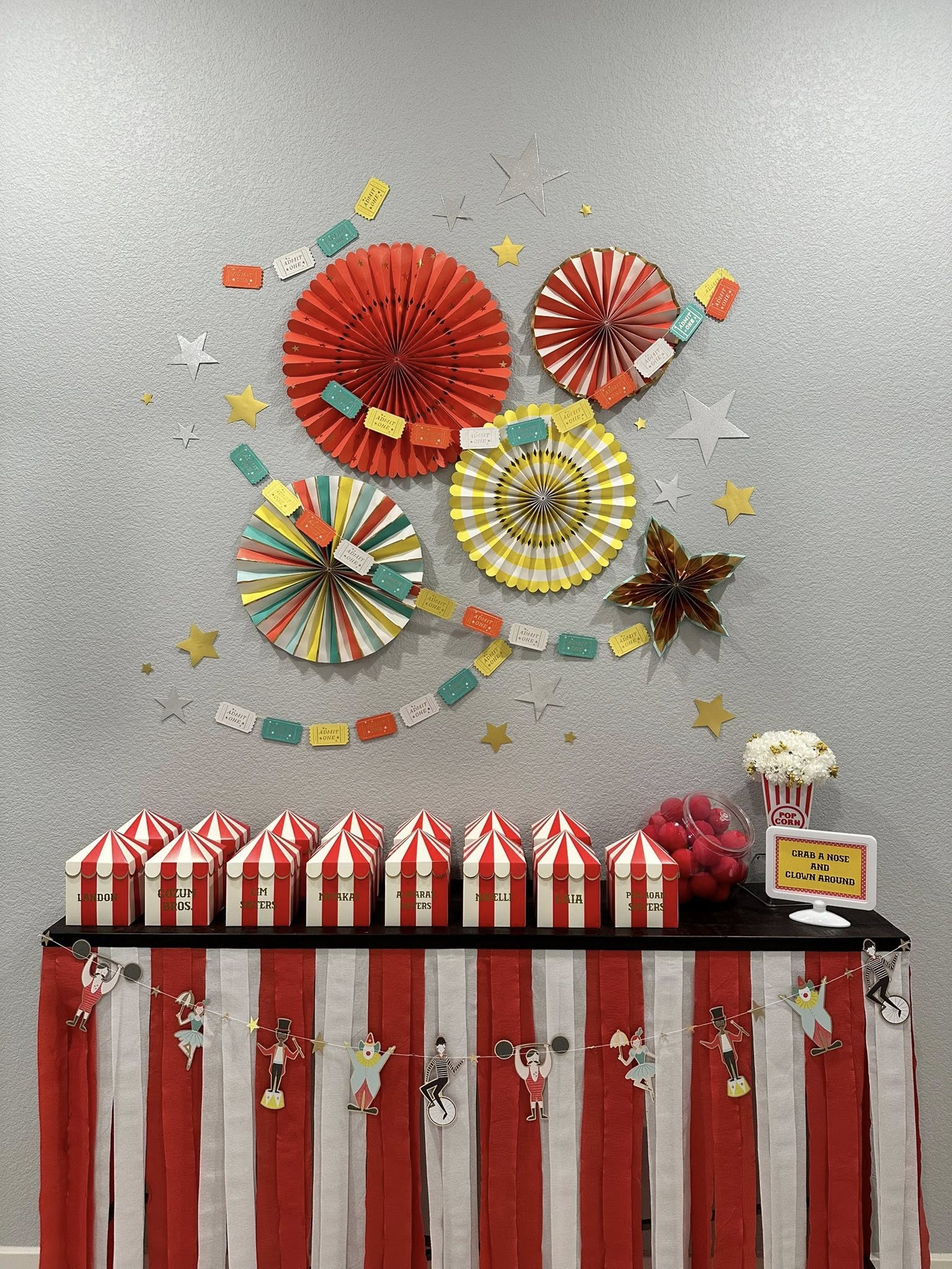 Table decorated for a circus themed party with red and white striped boxes, a banner, and paper fan wall decor.
